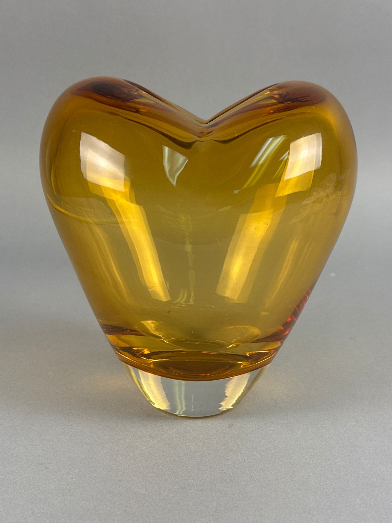 Amber Art Glass Heart-Shaped Vase: An elegant mid-century modern style sculptural vase. This piece is executed using the sommerso technique, featuring a vibrant honey-amber core submerged within a thick, heavy clear glass casing. The h