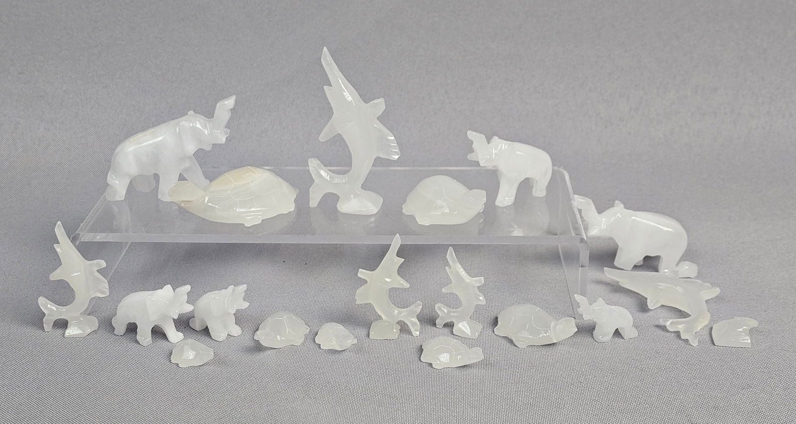 An Assortment of Miniature Carved Onyx Stone Animal Figurines: An assortment of animal figurines carved from a translucent white stone. The collection features stylized representations of elephants, turtles, and marlins. Each piece is hand-carved with simplified,