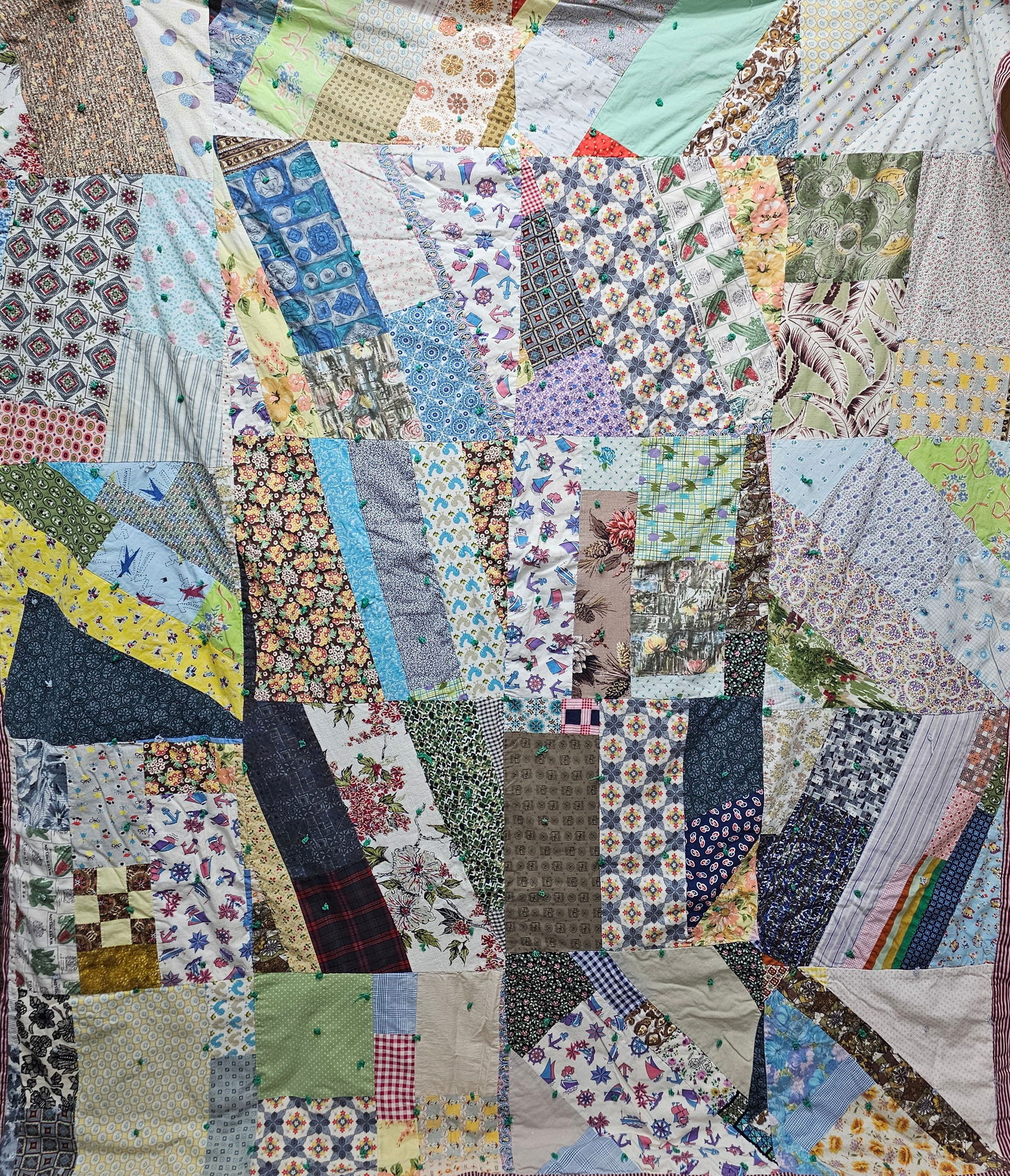 Handmade Patchwork Crazy Quilt: This handmade crazy quilt style comforter or lap blanket features a multi-patterned patchwork top. The assembly includes a diverse collection of mid-20th century cotton and synthetic fabric scraps, sh