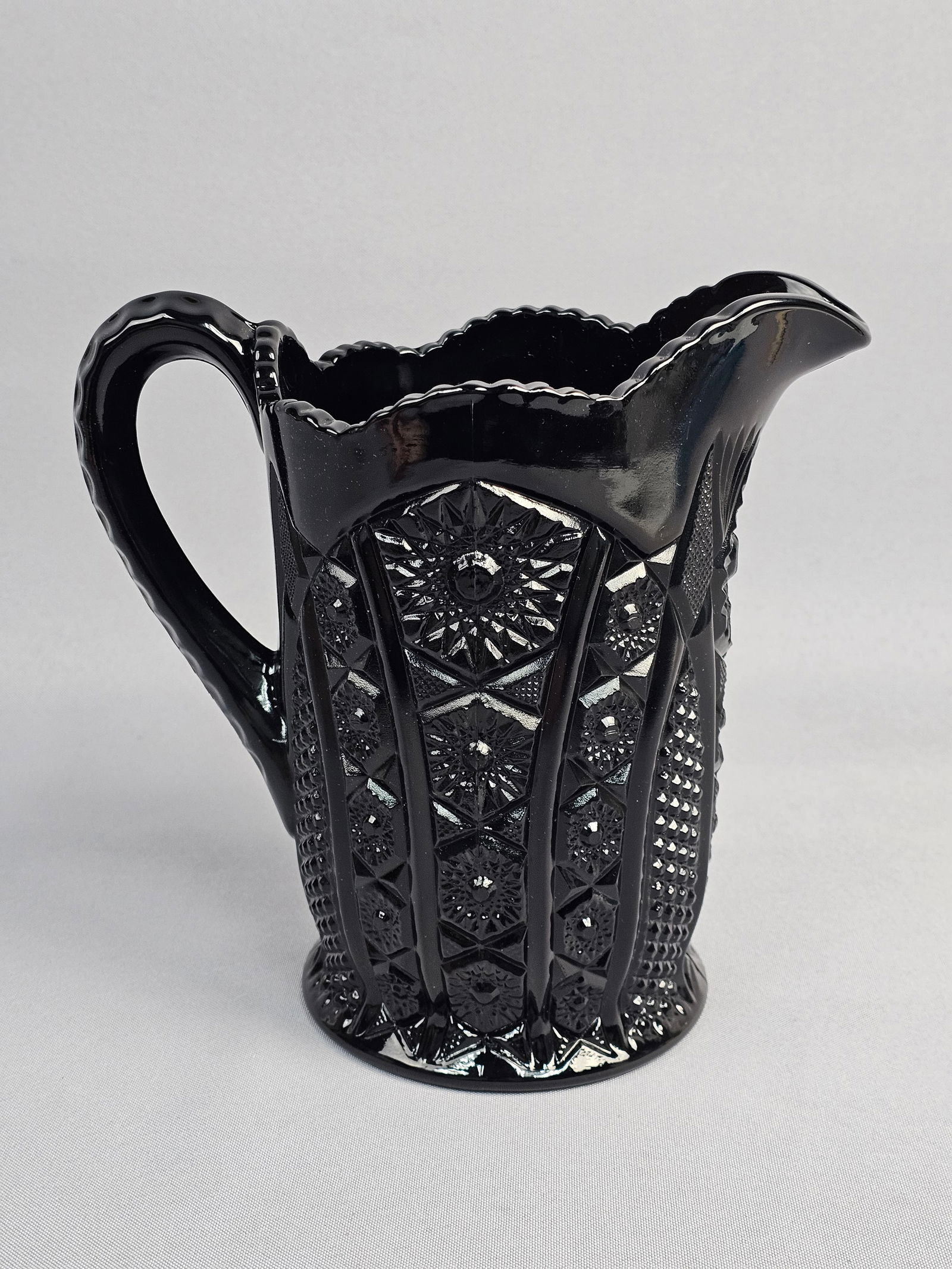 Indiana Glass for Tiara Exclusives Monarch Pattern Black Glass Pitcher: This pressed glass pitcher is attributed to Indiana Glass as part of the Monarch pattern produced for Tiara Exclusives during the late 20th century. The piece is crafted in opaque black glass, often r