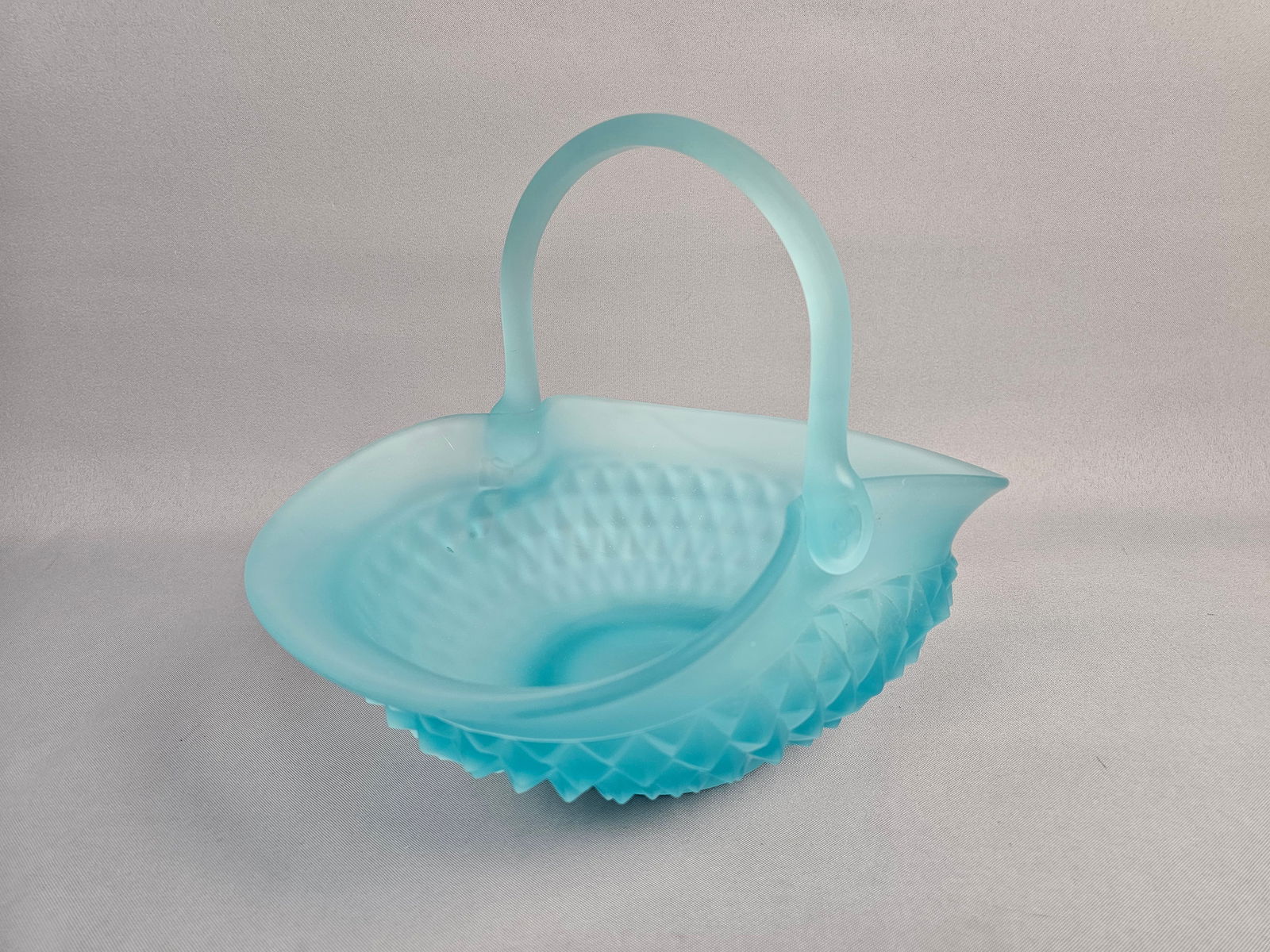 Vintage Tiara Exclusives Art Glass Aquamarine Satin Glass Basket: The piece features a soft, frosted satin finish achieved through acid-etching on a pressed glass body. The exterior is decorated with a geometric diamond-point or hobnail-style pattern. The basket is