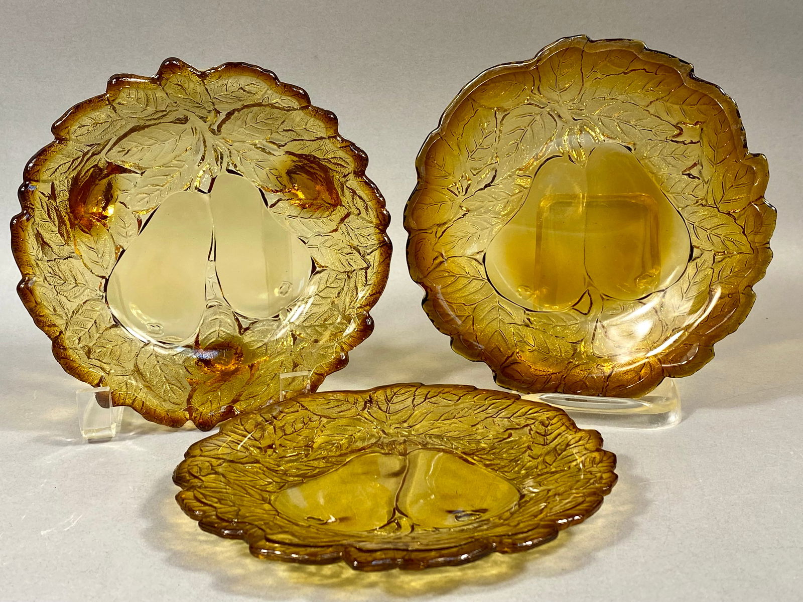 Attributed to Indiana Glass, Pressed Amber Glass, Three Fruit Motif Dishes: A set of three mid-century American pressed glass dishes in a rich translucent amber color, often referred to as "Burnt Honey." This set is attributed to the Indiana Glass Company, likely pr