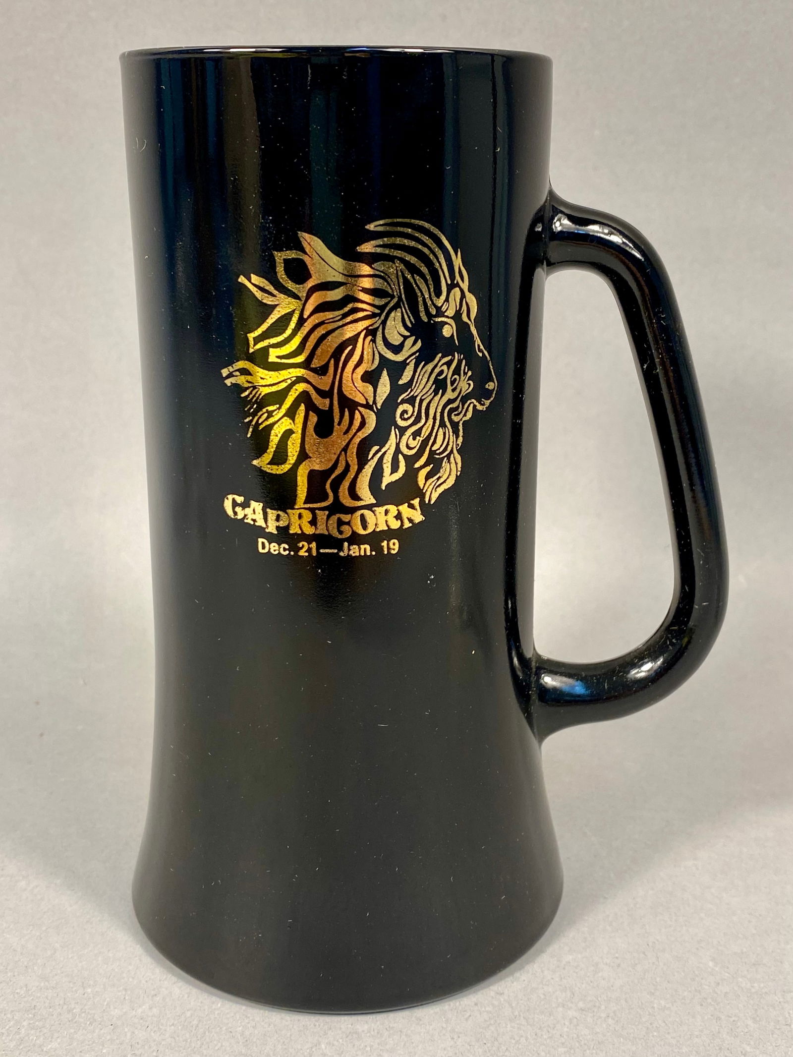 Tiara Exclusives, Pressed Black Glass Capricorn Zodiac Mug: This vintage mug was produced by Indiana Glass for Tiara Exclusives. The piece is crafted from opaque black glass, commonly known as "Ebony" or "Black Amethyst" glass. The vessel f