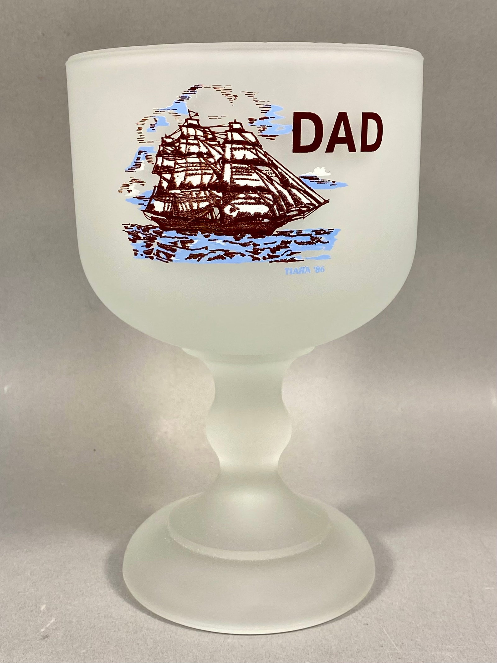 Tiara Exclusives Sailing Ship Dad Schooner, 1986: This vintage frosted satin glass schooner was produced by Tiara Exclusives. The front of the vessel features a graphic of a three-masted sailing ship rendered in brown and blue tones, with the word DA