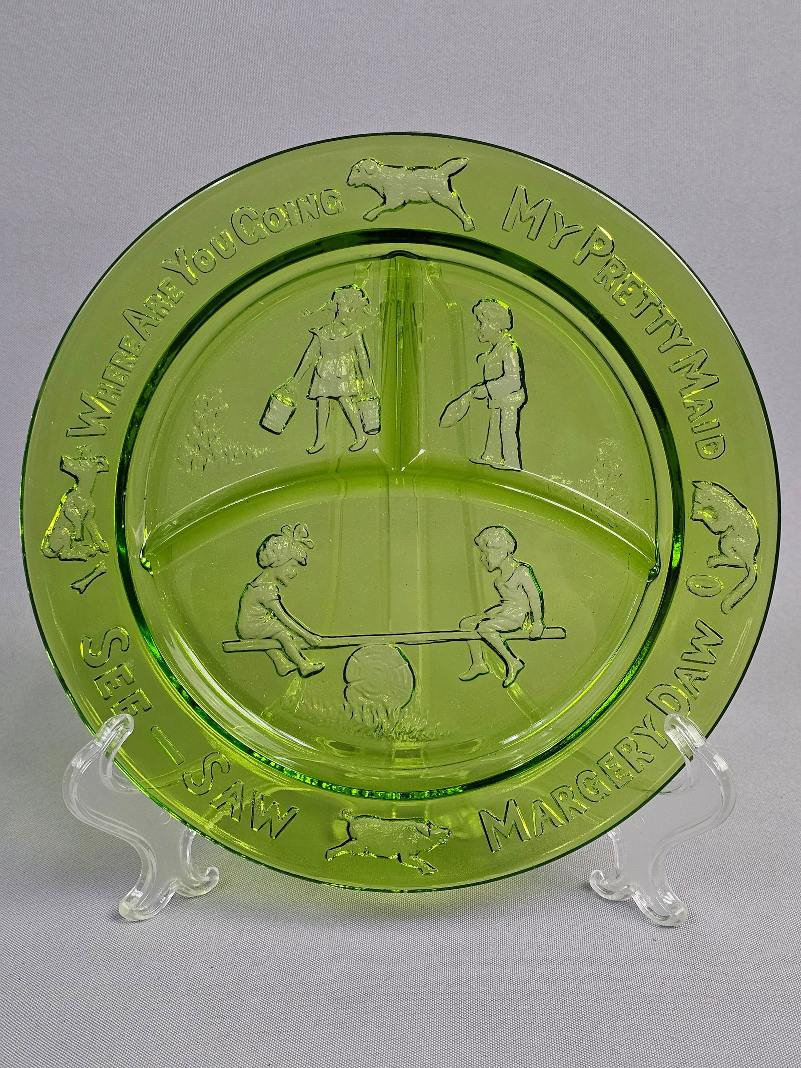 Green Pressed Glass Nursery Rhyme Pattern Child's Divided Plate: This child's divided plate is crafted from transparent green pressed glass, attributed to the Indiana Glass Company for the Tiara Exclusives line. The circular form is divided into three compartments