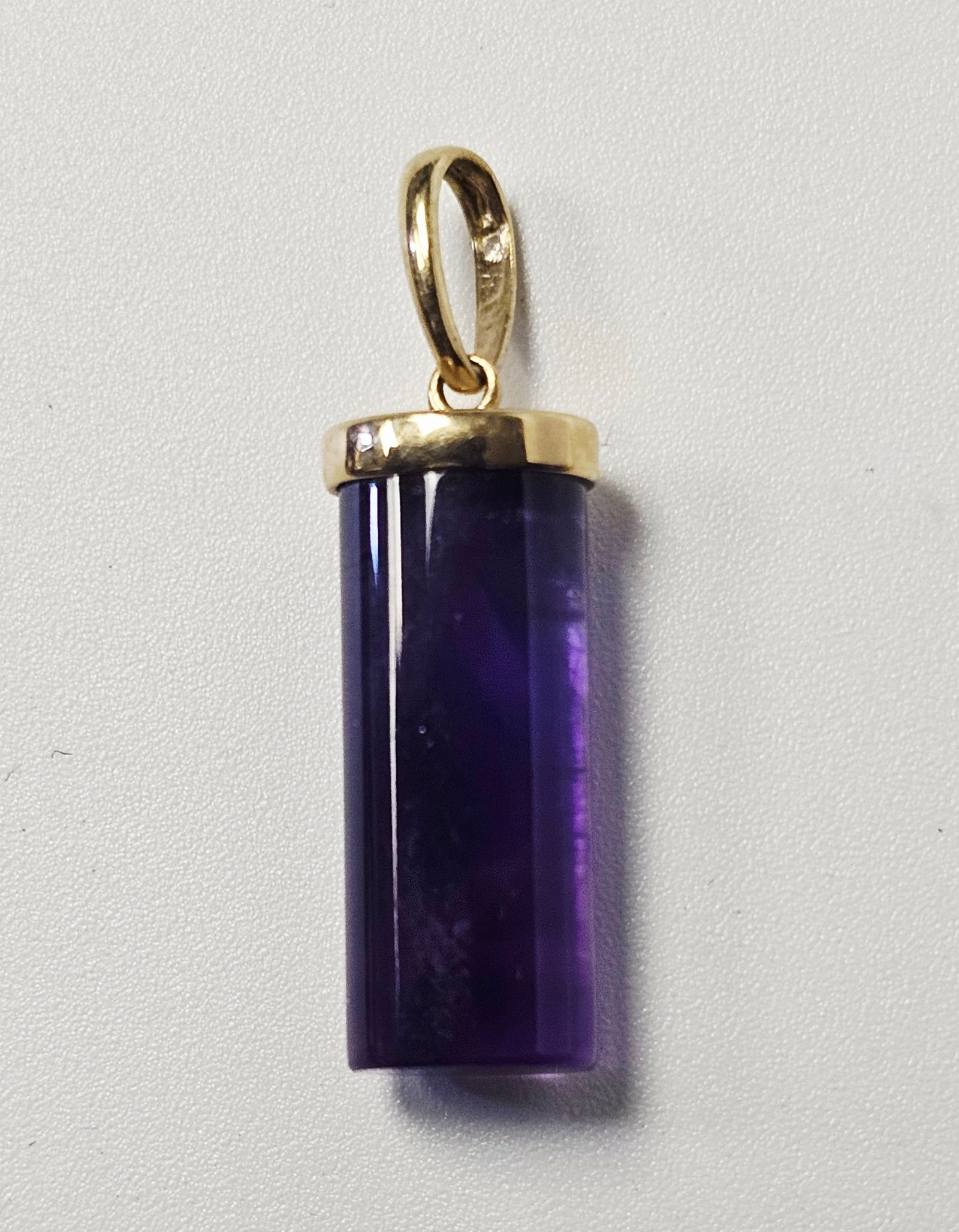 10K Gold & Amethyst Prism Pendant: This jewelry item is a pendant featuring a carved amethyst gemstone in a faceted cylindrical prism form. The stone is secured by a 10 karat yellow gold cap-style setting. The setting is connected to a