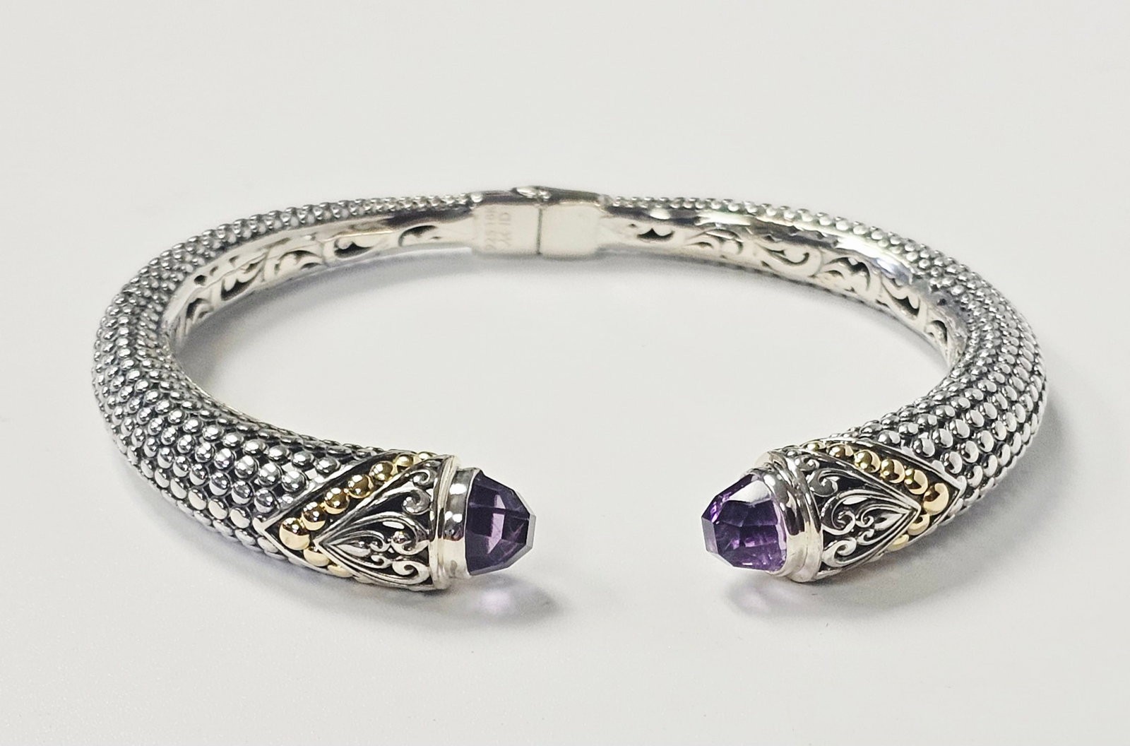 Sterling & 18K Gold Bracelet Amethyst-Colored Gemstones 25.7 Grams: This two-tone hinged cuff bracelet features a textured, beaded body transitioning into ornate terminals decorated with silver scrollwork and 18 karat gold granulated accents. Each terminal is set with