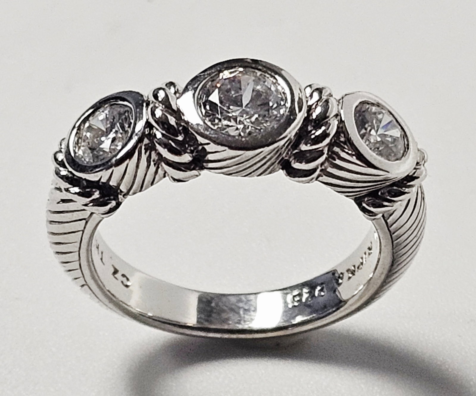 Judith Ripka Sterling Cubic Zirconia Ring 6.1 Grams: This ring is designed by Judith Ripka and crafted in sterling silver. The design features three graduated, round faceted clear cubic zirconia stones, each secured in a bezel setting. The band and sett