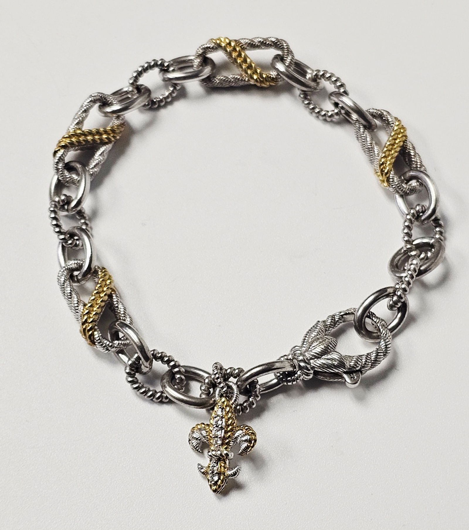 Judith Ripka Sterling Fleur-de-lis Link Bracelet 27.7 Grams: A designer link bracelet by Judith Ripka crafted in sterling silver with yellow gold-tone accents. The piece features alternating polished oval links and larger, textured rope-style links with gold-to