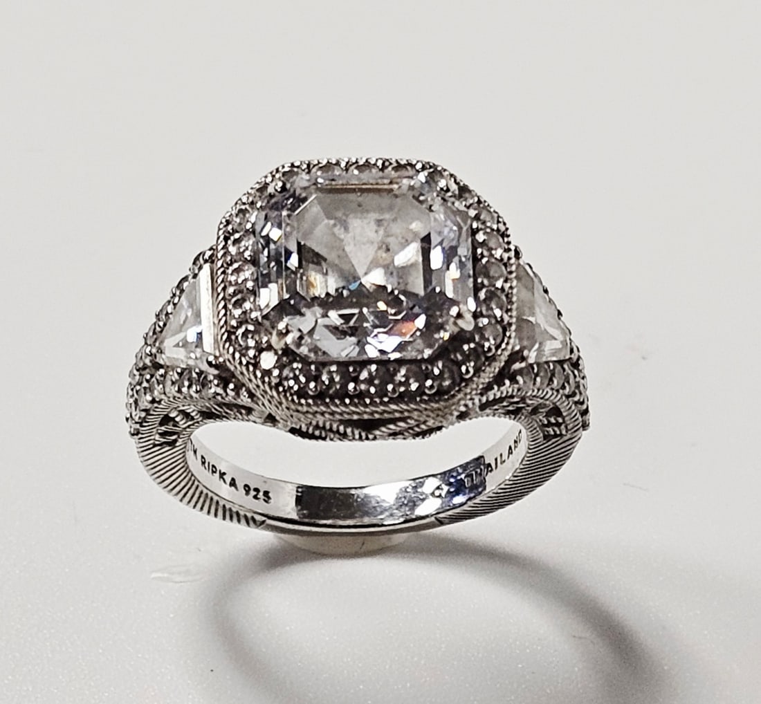 Judith Ripka Sterling Cubic Zirconia Cocktail Ring 7.8 Grams: A sterling silver cocktail ring by designer Judith Ripka. The piece features a central square step-cut cubic zirconia in a prong setting, surrounded by a halo of round-cut cubic zirconia accents. The