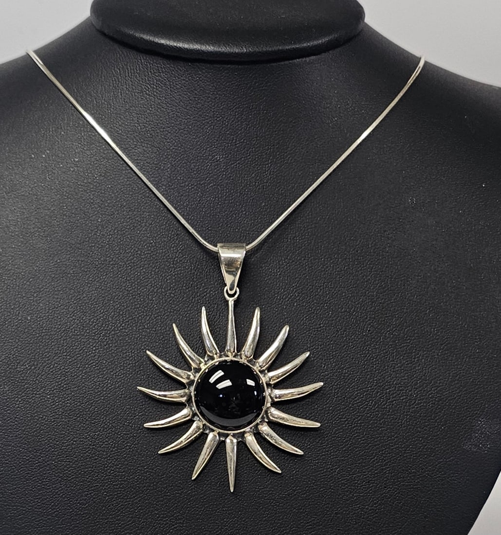 Sterling Black Onyx Sunburst Pendant Necklace 24.9 Grams: This jewelry lot features a sterling silver pendant designed in a sunburst motif suspended from a fine snake chain. The pendant centers a large round black onyx cabochon, which is bezel-set within a f
