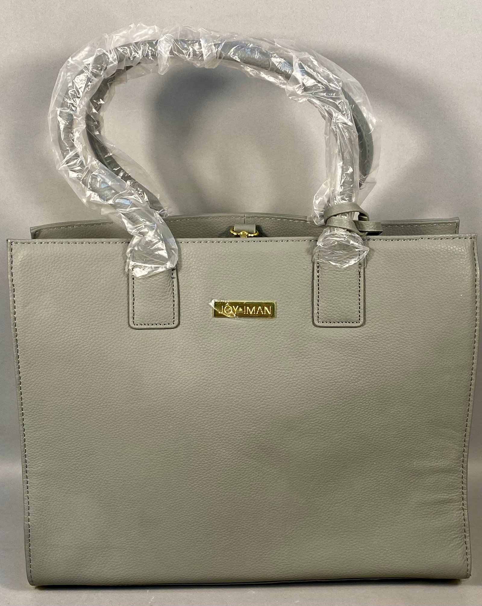 Joy and Iman Gray Pebble Grained Leather Multi Compartment Tote Bag: A structured tote bag by Joy and Iman crafted from gray pebble-grained leather with gold-tone hardware. The exterior features dual rolled top handles and a rear zippered pocket. The front is detailed