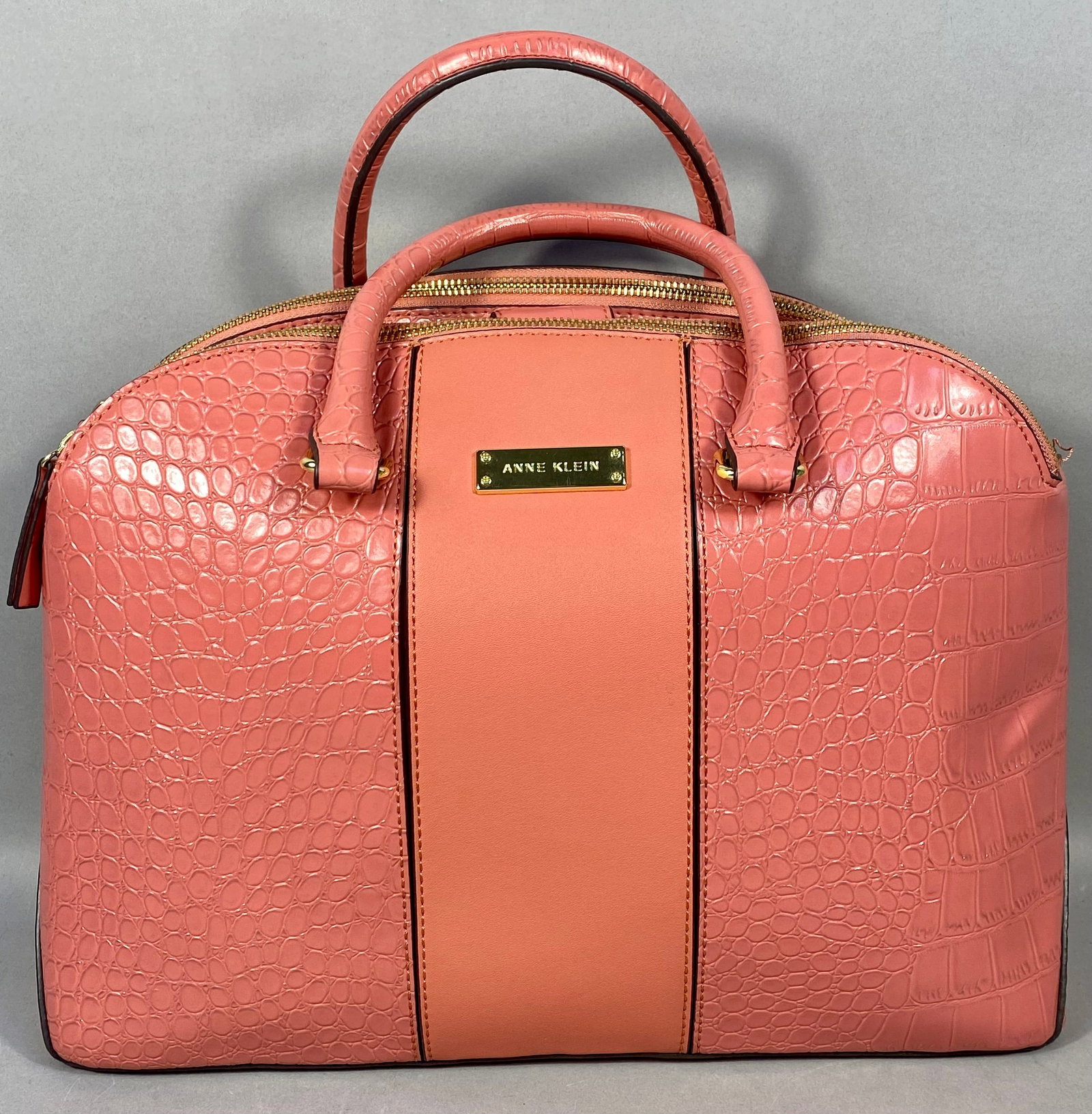 Anne Klein Coral Pink Crocodile Embossed Triple Compartment Dome Satchel: An Anne Klein dome satchel constructed from coral pink synthetic leather. The exterior features a combination of crocodile-embossed and smooth panels. The bag is designed with a triple-compartment int
