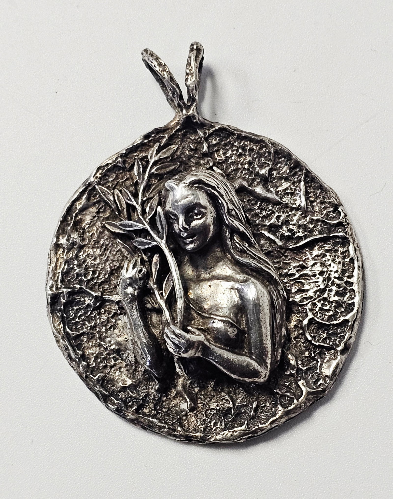 Sterling Figural Medallion Pendant 28.4 Grams: A sterling silver medallion pendant featuring a high-relief sculptural design of a woman with long, flowing hair holding a leafy branch. The circular pendant is characterized by a heavily textured, ru