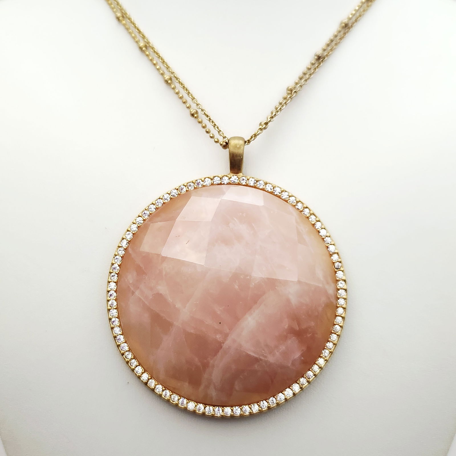Sheila Fajl Gold-Tone Rose Quartz Pendant Necklace: A fashion necklace from the Glow by Sheila Fajl collection featuring a large circular pendant. The pendant is set with a faceted rose-pink stone, likely rose quartz, bordered by a halo of small clear
