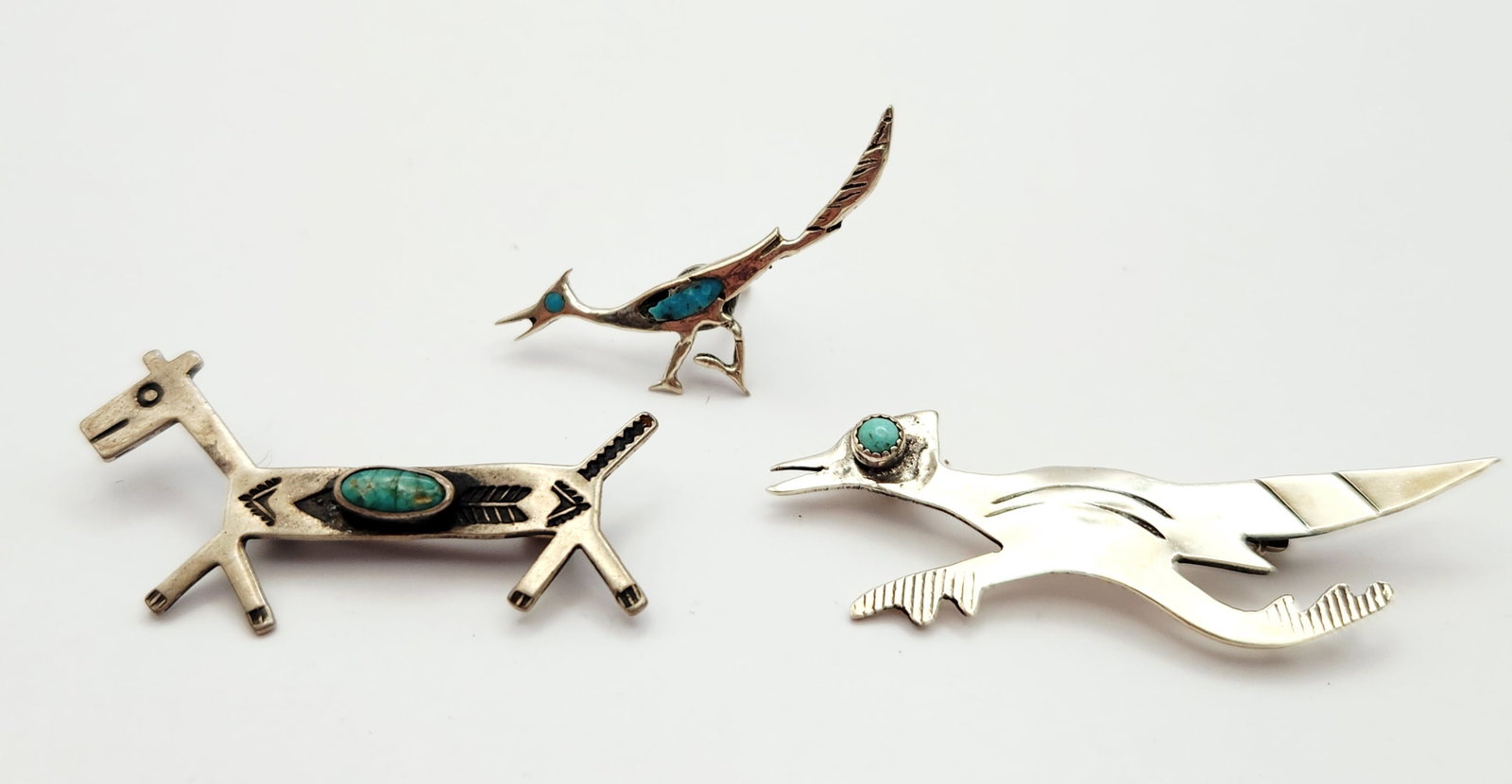 Southwestern Sterling Turquoise Pins 6.7 Grams: A trio of silver-toned metal pins featuring Southwestern motifs. The first item is a stylized four-legged animal pin, possibly a horse or deer, set with a central oval cabochon of what appears to be t