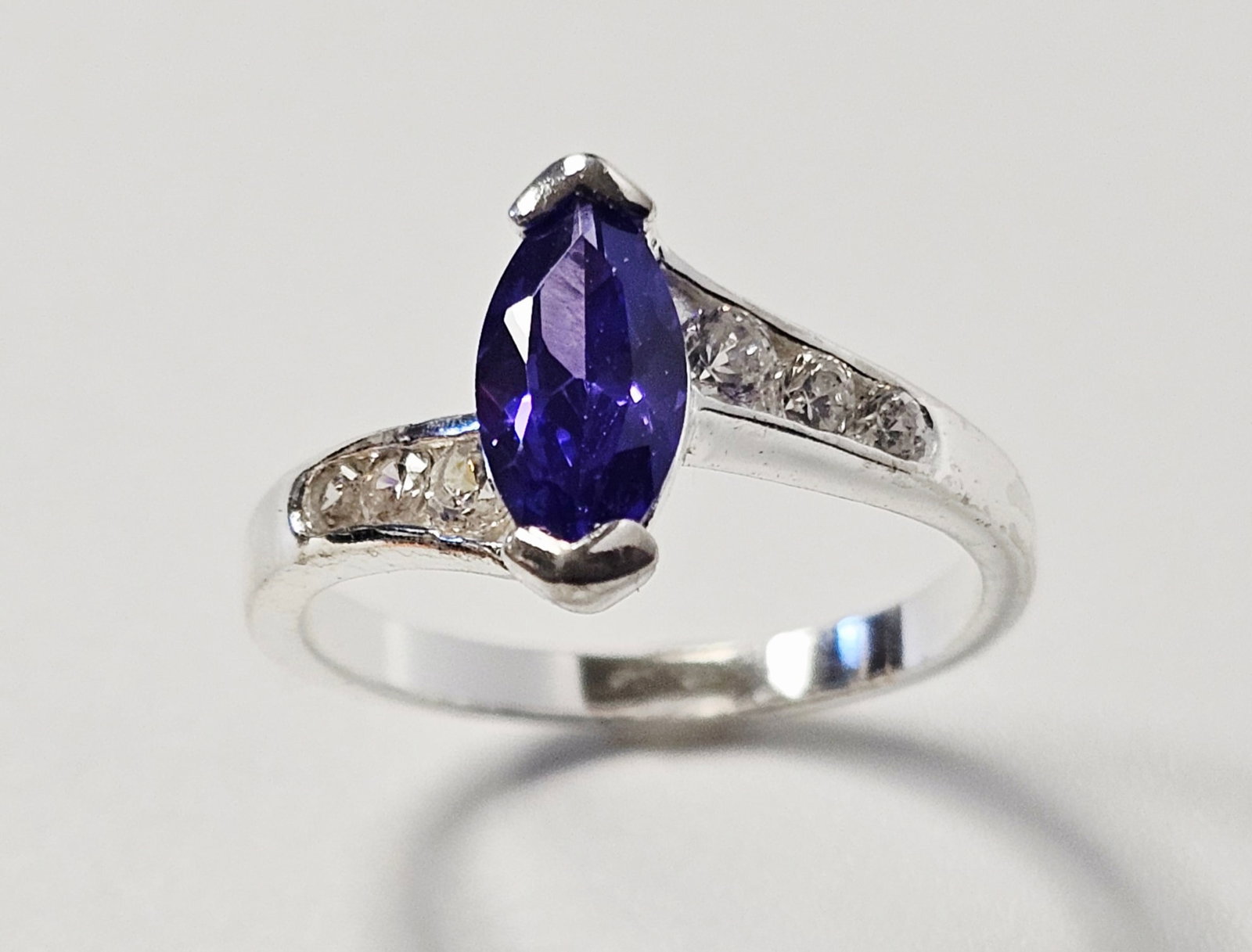 Sterling Marquise Cut Purple Stone Ring 3.3 Grams: This fashion ring is constructed from white metal and features a bypass-style design. The center of the ring is set with a single marquise-cut purple stone, held in place by two V-prongs at the tips.