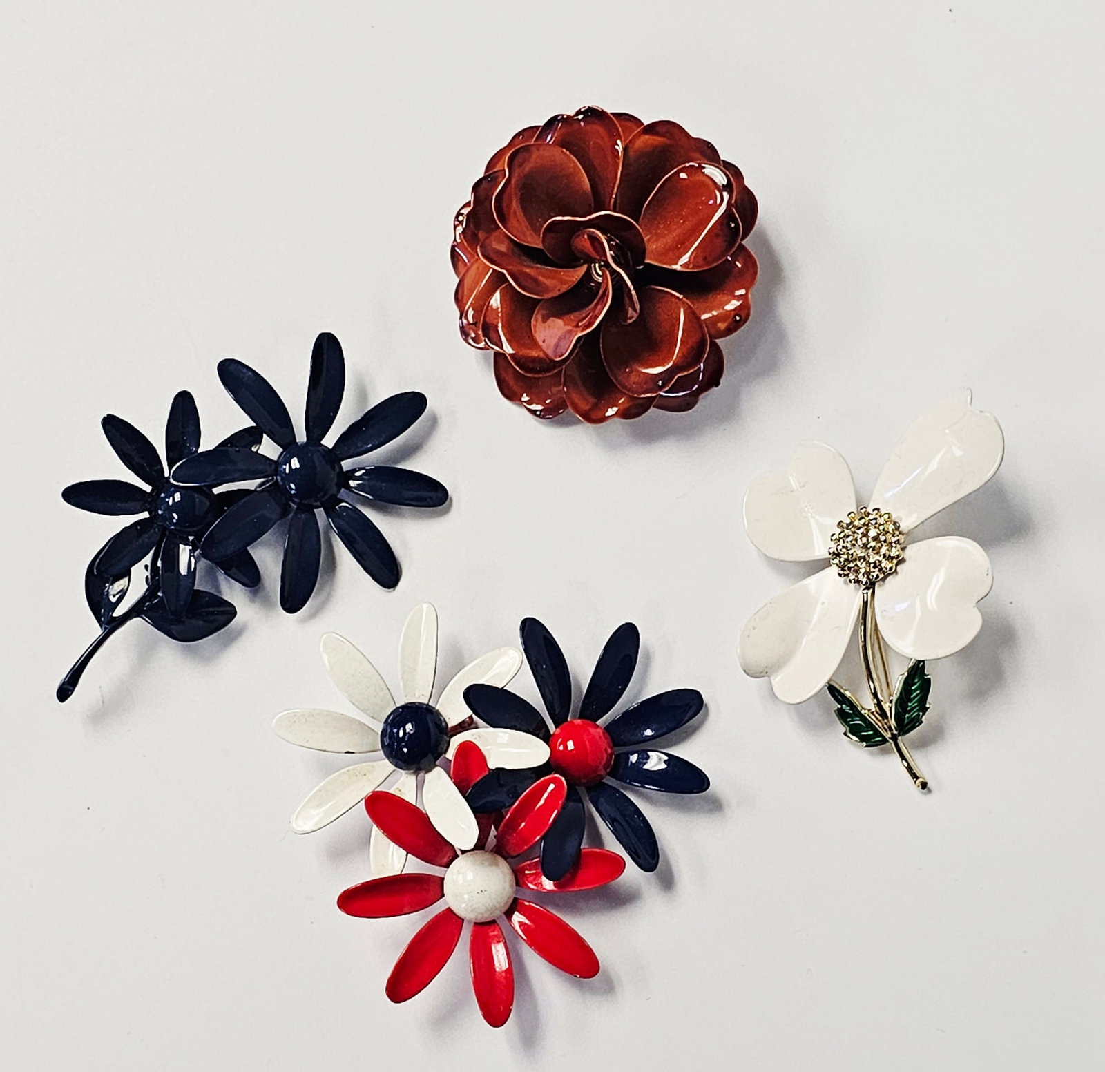Vintage Enameled Floral Brooches: This collection features several mid-century style costume jewelry brooches with various floral motifs and enamel finishes on base metal. The assortment includes a blue enameled double daisy brooch on