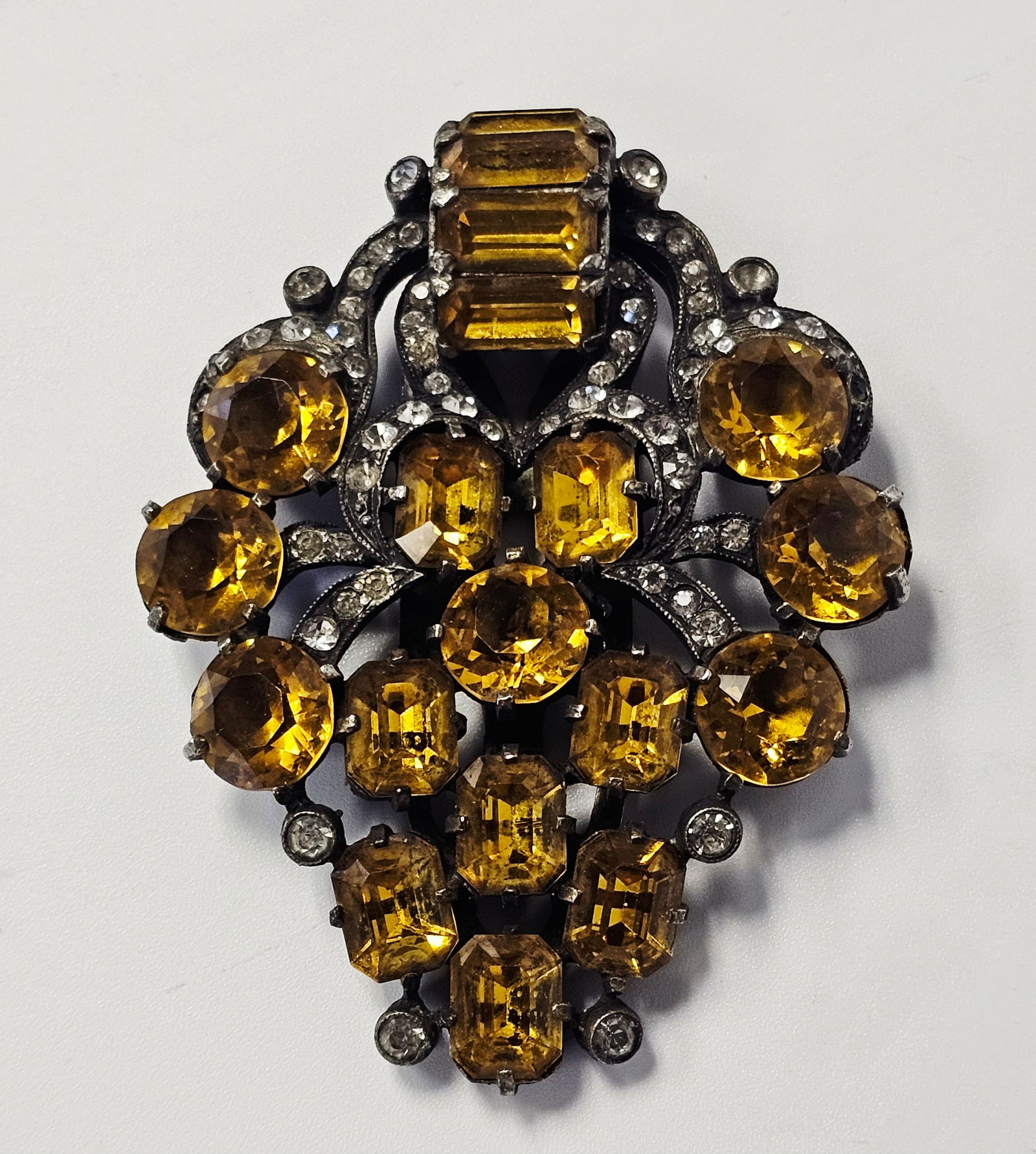 Eisenberg Original Citrine Glass & Rhinestone Dress Clip: This dress clip is a product of the American firm Eisenberg and Sons. The piece features an ornate shield-shaped cluster design with scrolled accents. It is constructed from silver-tone metal with a d