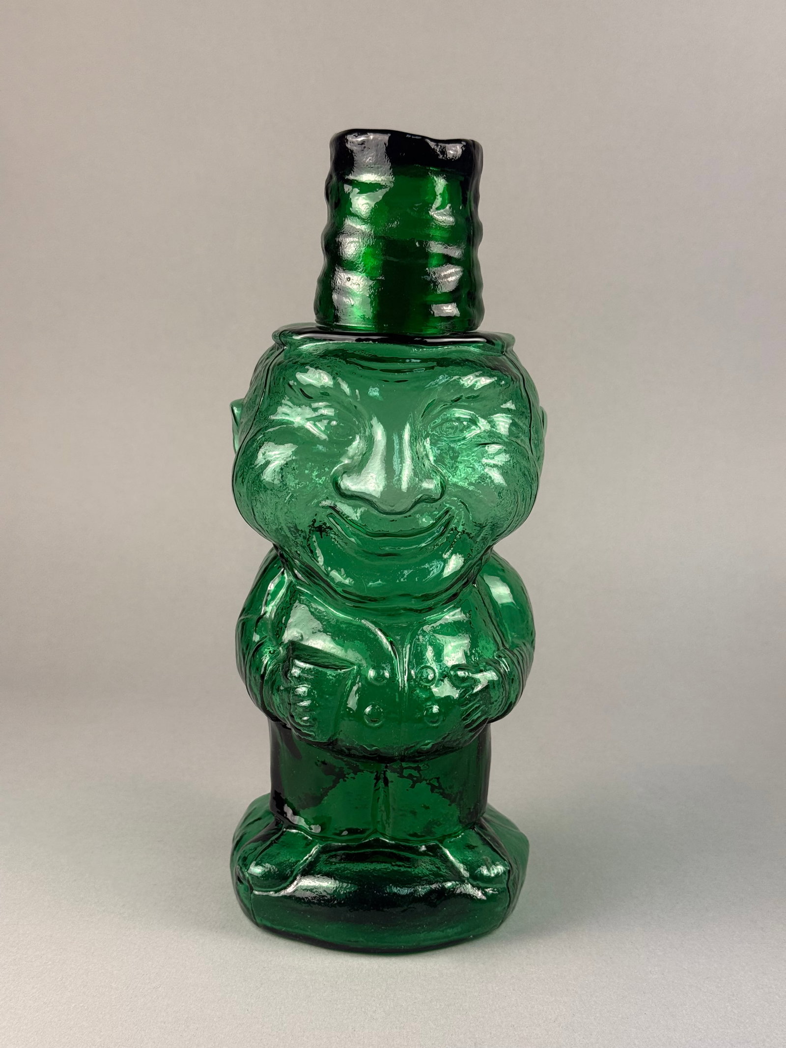 Emerald Green Indiana Glass Jolly Mountaineer Figural Decanter w Shot Glass: A two-piece molded glass figural decanter in a deep emerald green color, distributed by Tiara Exclusives. The set consists of a bottle base and a coordinating glass cap designed to function as a shot