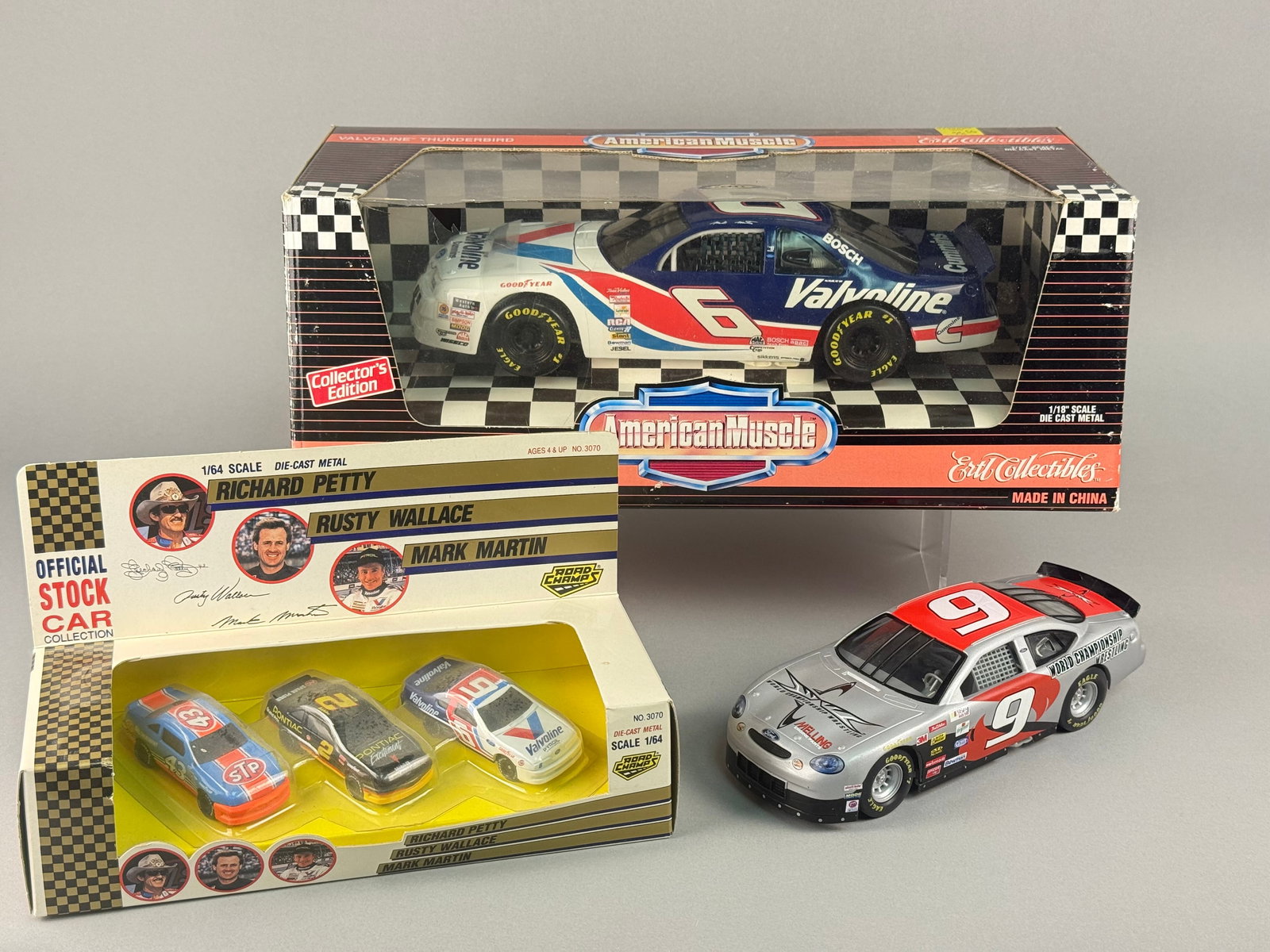 A Collection of NASCAR Die-Cast Model Cars Including Ertl American Muscle and Road Champs: A collection of NASCAR-themed die-cast model cars featuring various scales and manufacturers. The group includes a 1/18 scale Mark Martin #6 Valvoline Ford Thunderbird from the American Muscle series