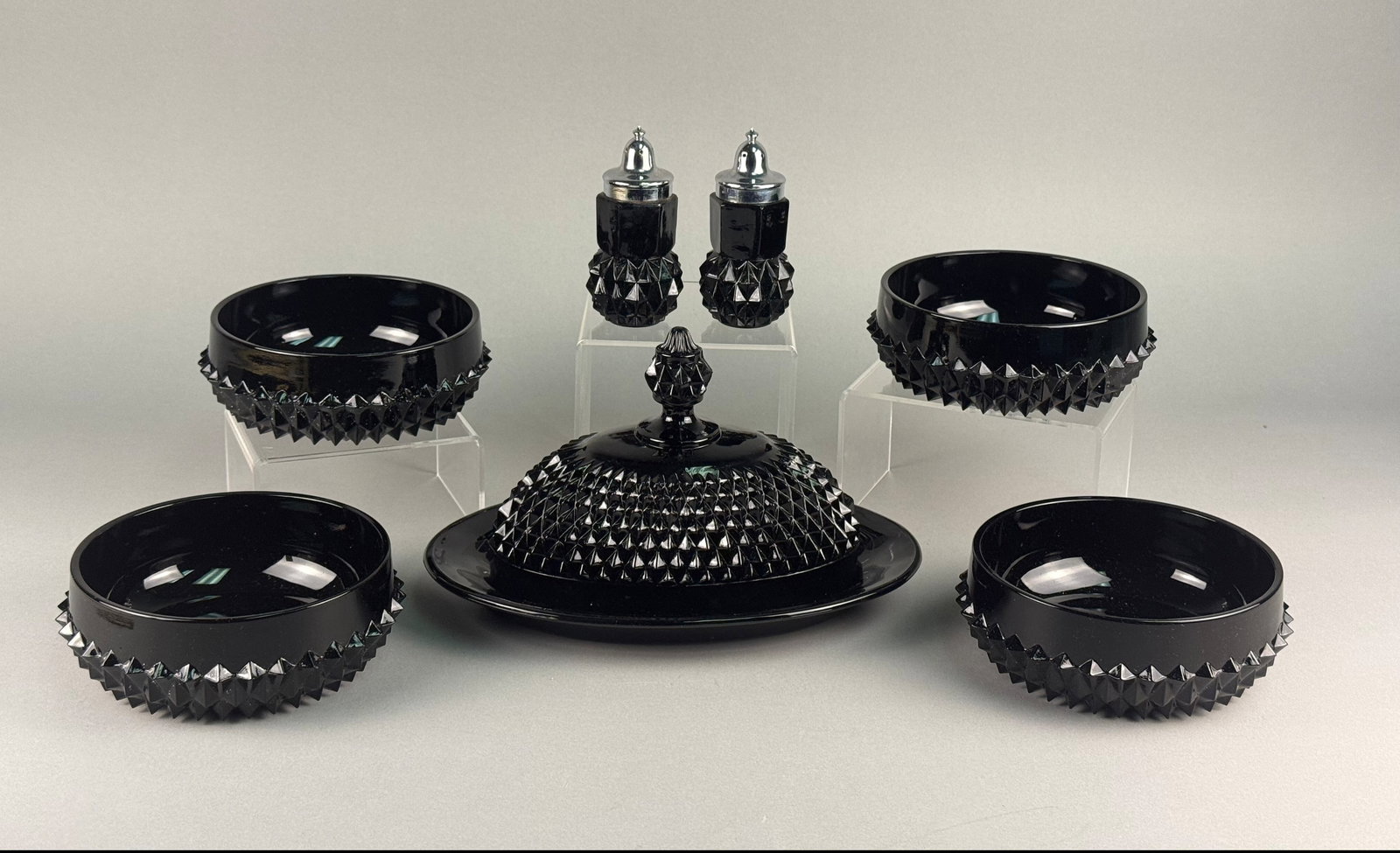 Tiara Exclusives, Pressed Black Amethyst Glass Tableware Set: This is an eight-piece set of opaque black amethyst glass tableware produced for Tiara Exclusives in the Cameo or Diamond Point pattern. The design is defined by a sharp, mold-pressed diamond point te