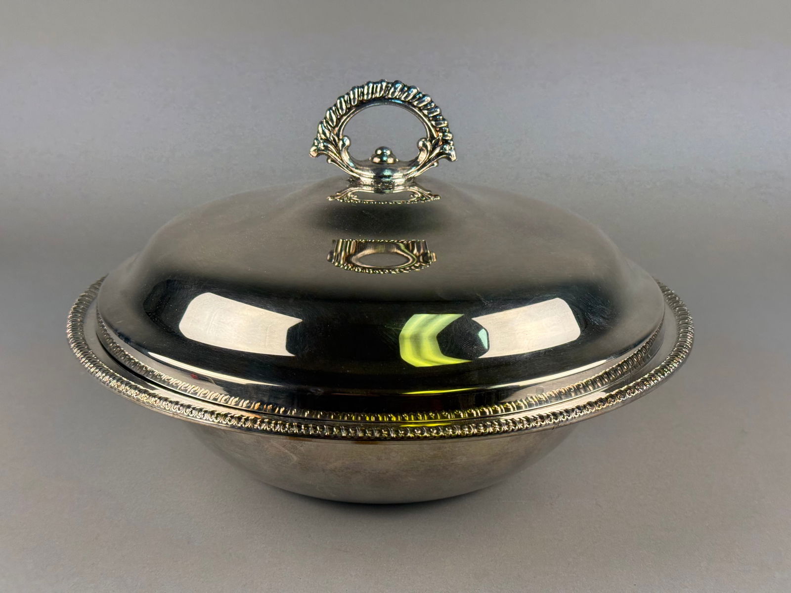 Rogers Silver-Plated Lidded Serving Dish with Pyrex Glass Liner: A silver-plated lidded serving dish with a clear glass liner. The circular metal base and dome-shaped lid feature a decorative gadrooned border. The lid is surmounted by an ornate foliate-style handle