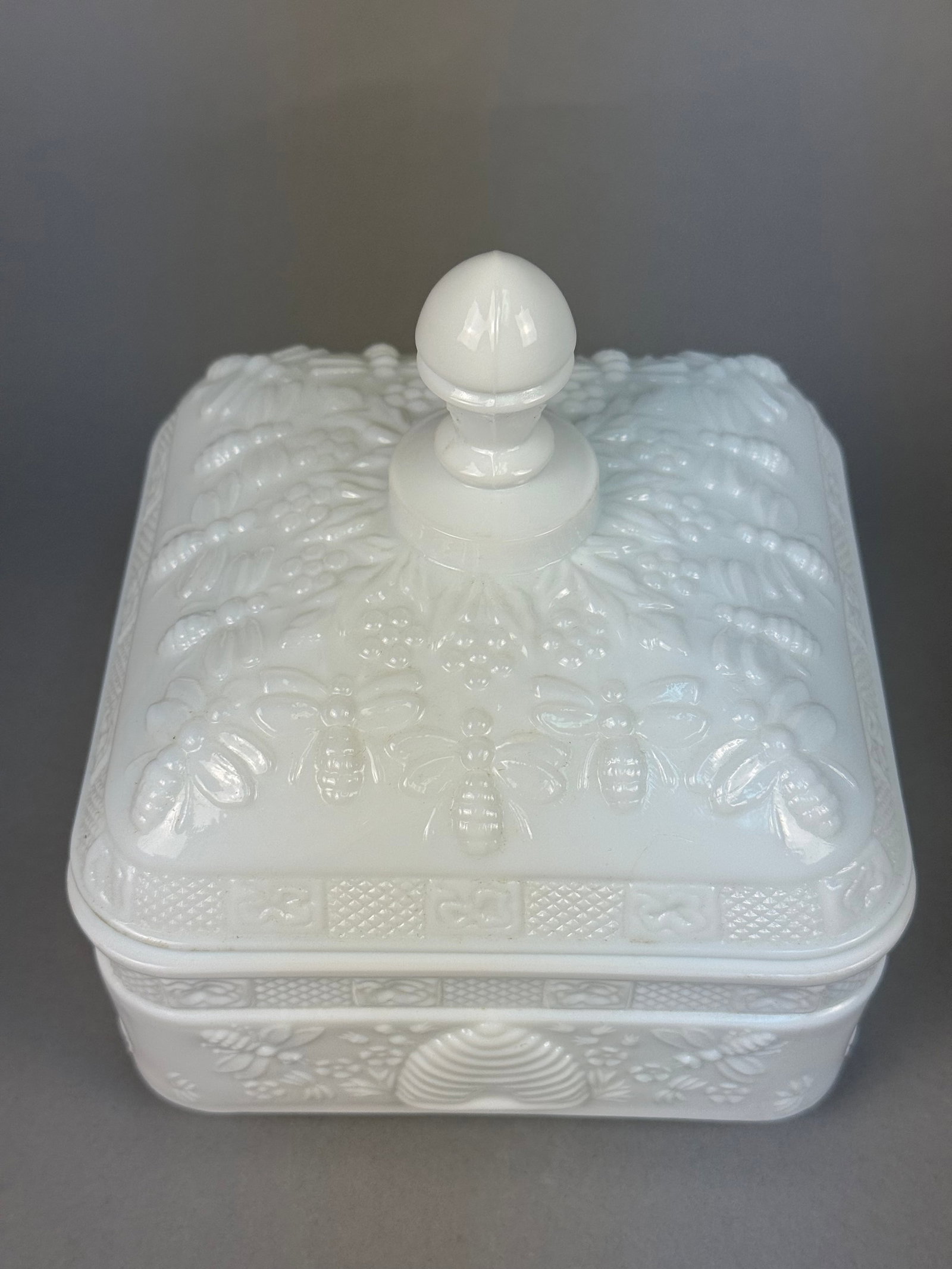 Tiara Glassware Honey Bee Pattern Milk Glass Lidded Box: Attributed to Tiara Glassware in the Honey Bee pattern, this rectangular lidded box is crafted from opaque white milk glass. The piece features relief-molded decoration throughout, including numerous