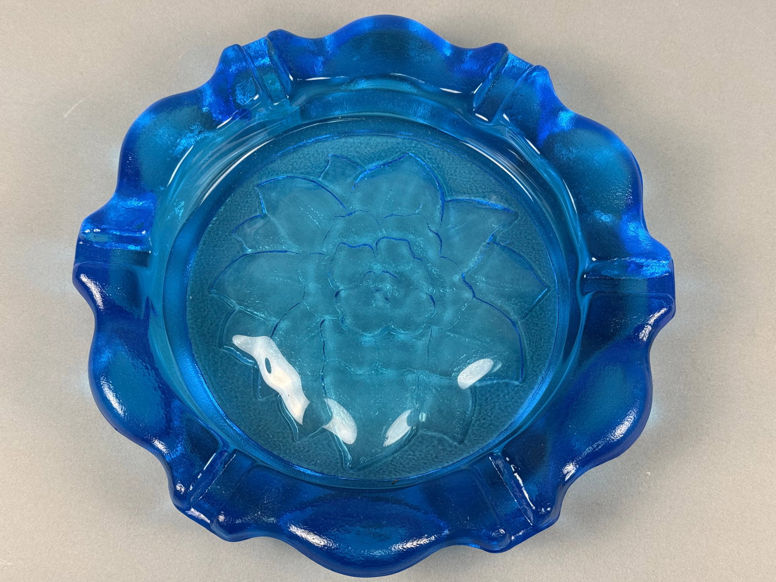 Large Cobalt Blue Pressed Glass Lotus Flower Ashtray by Tiara Exclusives: This large pressed glass ashtray is the Lotus Flower pattern produced by Indiana Glass for Tiara Exclusives. The piece is constructed from heavy cobalt blue glass and features a central embossed flora