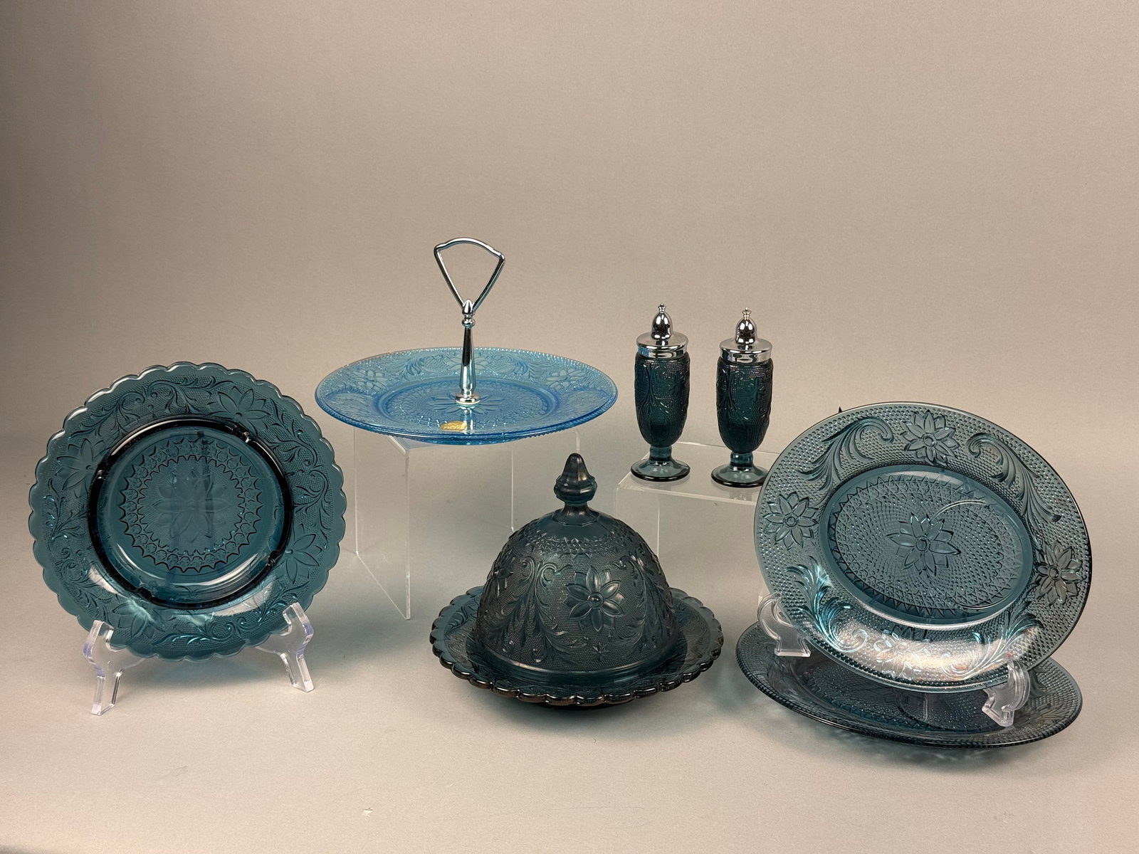 A Collection of Tiara Exclusives Sandwich Pattern Blue Glass Tableware: This collection of pressed glass tableware is produced in the Sandwich pattern, which features intricate floral and scroll motifs on a stippled ground. These items were marketed by Tiara Exclusives an