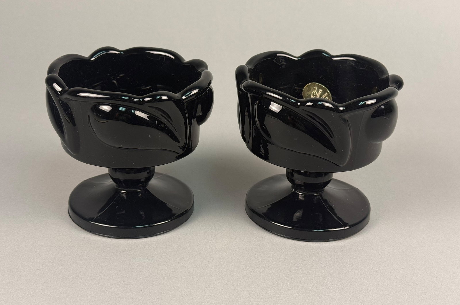 A Pair of Tiara Exclusives Mt. Pleasant Pattern Black Glass Candle Holders: This pair of pedestal candle holders is produced in the Mt. Pleasant pattern for Tiara Exclusives. The items are constructed from opaque black glass, also known as black amethyst or ebony glass. Each