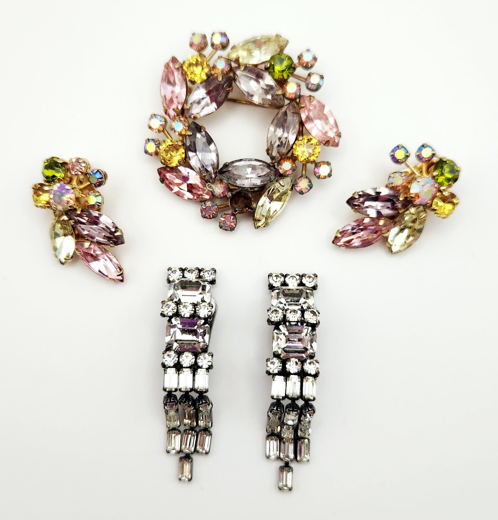 Weiss Rhinestone Brooch & Clip-on Earrings: A collection of Weiss costume jewelry including a multi-colored rhinestone wreath brooch and two pairs of clip-on earrings measuring between 1.25 and 2 inches. The brooch is missing a stone, see pict
