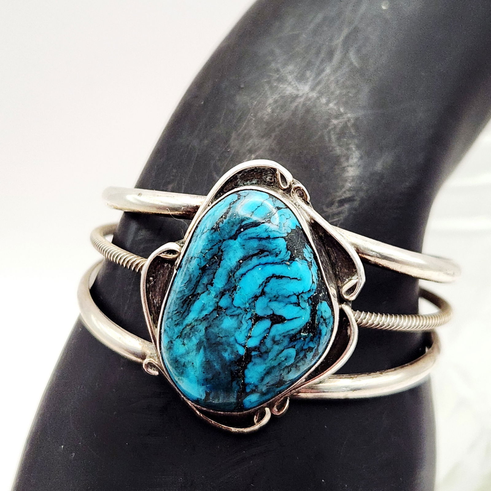 Sterling Turquoise Bracelet 25.1 Grams: This cuff bracelet is crafted from sterling silver and features a large, bezel-set cabochon that appears to be turquoise with a prominent black matrix. The triple-shank cuff is constructed with two ou