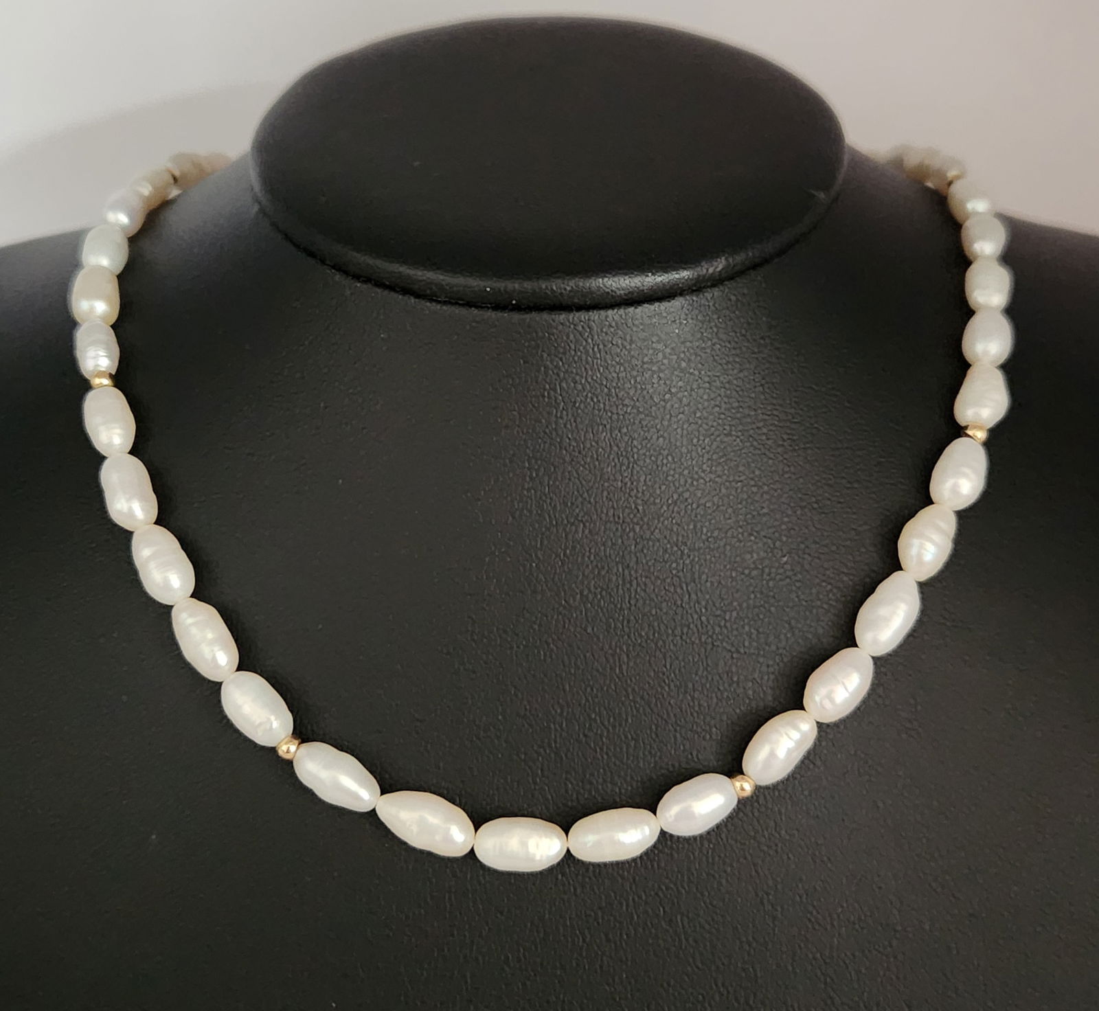 14K Gold Pearl Necklace 18.1 Grams: This necklace is composed of a single strand of oval-shaped white cultured pearls interspersed with small yellow gold beads. The pearls measure approximately 8mm to 12mm in length. The strand is secur