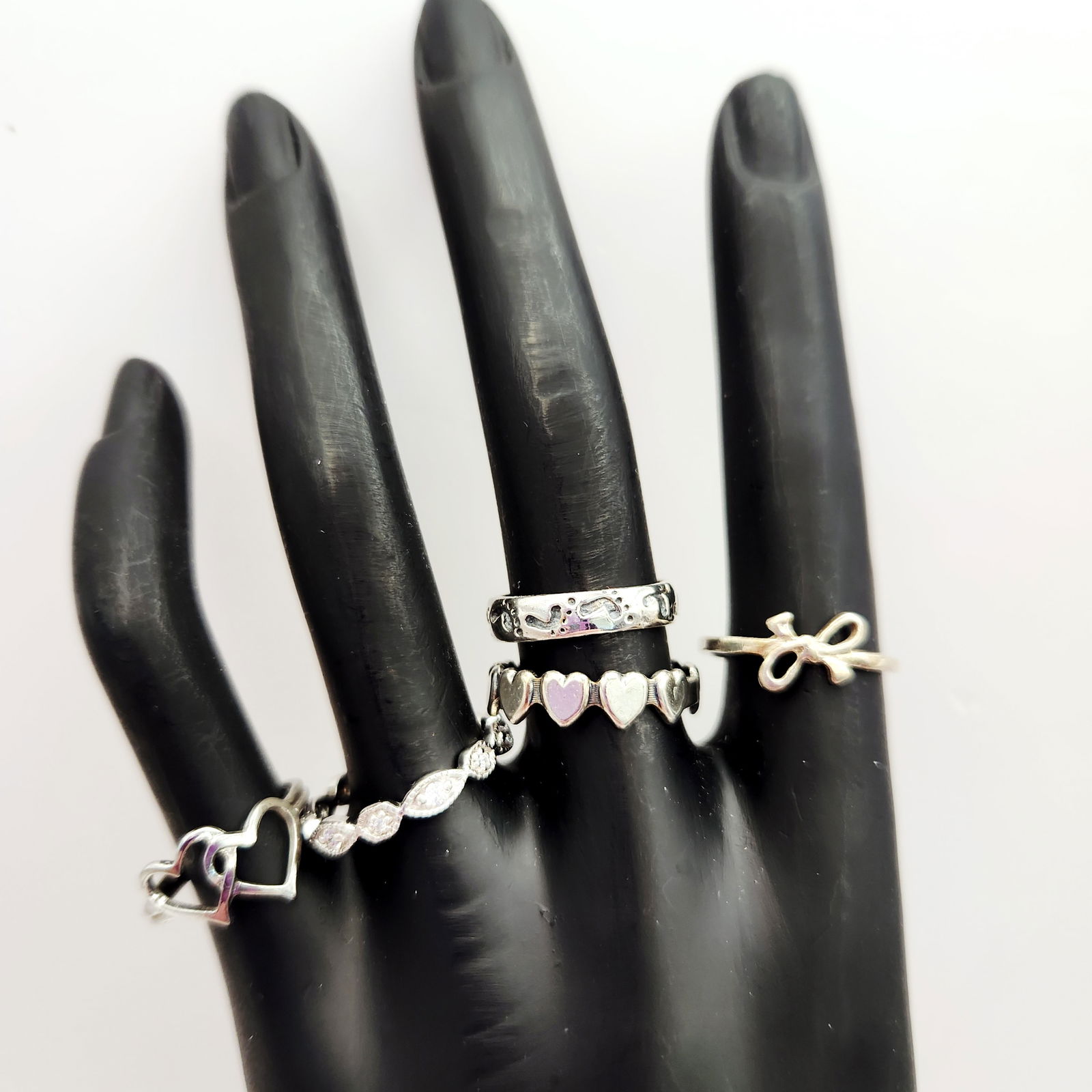 Five Sterling Silver Rings 9 Grams: A collection of five sterling silver rings featuring bow, footprint, and heart motifs, including one marked Beau Sterling and another with clear stone accents, weighing a total of 9 grams and ranging