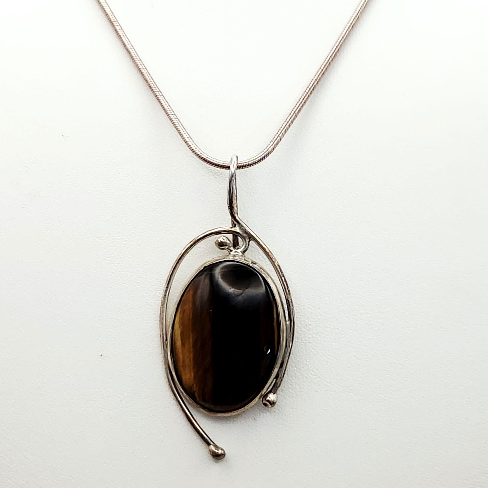 Sterling Tiger's Eye Necklace 18.6 Grams: A modernist studio jewelry necklace featuring a pendant by J. Sanford. The pendant consists of a large oval tiger's eye cabochon set within a stylized sterling silver frame featuring openwork wire des