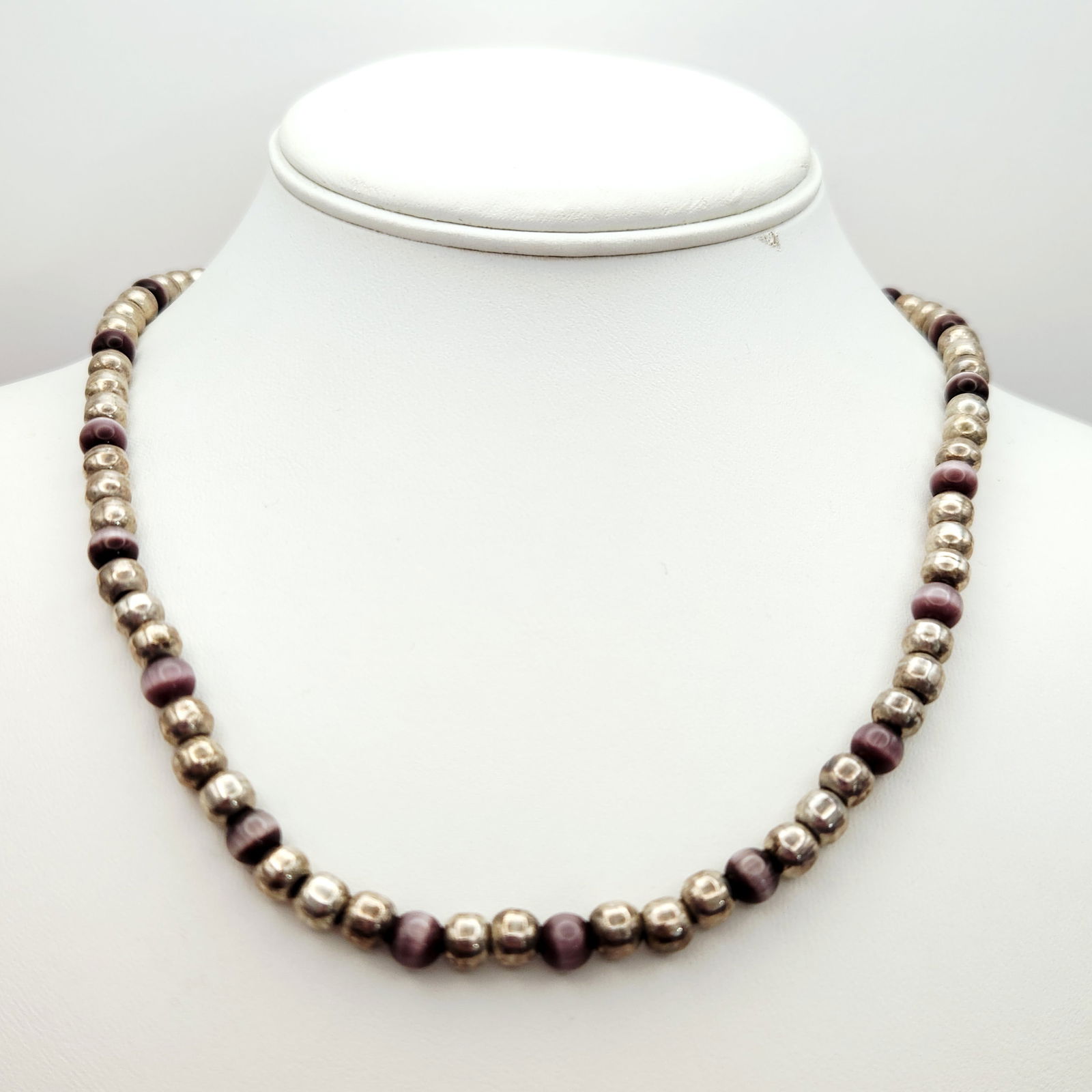 Sterling Purple Chatoyant Necklace 37.3 Grams: A beaded necklace featuring alternating round sterling silver beads and purple chatoyant beads. The chatoyant beads display a distinct cat's eye effect. The piece is constructed with a hook-and-eye cl