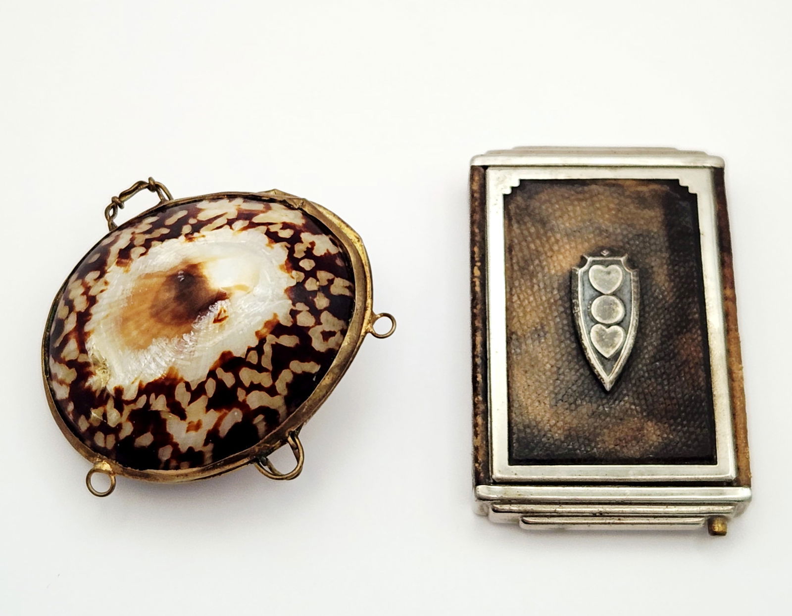 Vintage Cowrie Shell Case & Girey Makeup Compact: A vintage hinged cowrie shell case with brass fittings measuring approximately 2.5 inches long, alongside a Girey rectangular makeup compact with a textured brown cover and silver-tone heart emblem me