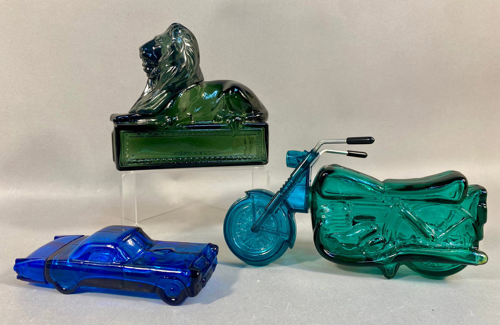 Three Vintage Avon Molded Glass Novelty Decanters: Three vintage Avon molded glass novelty decanters including a green lion, a blue '55 Thunderbird car, and a teal motorcycle, measuring approximately 4.5 to 7 inches.
