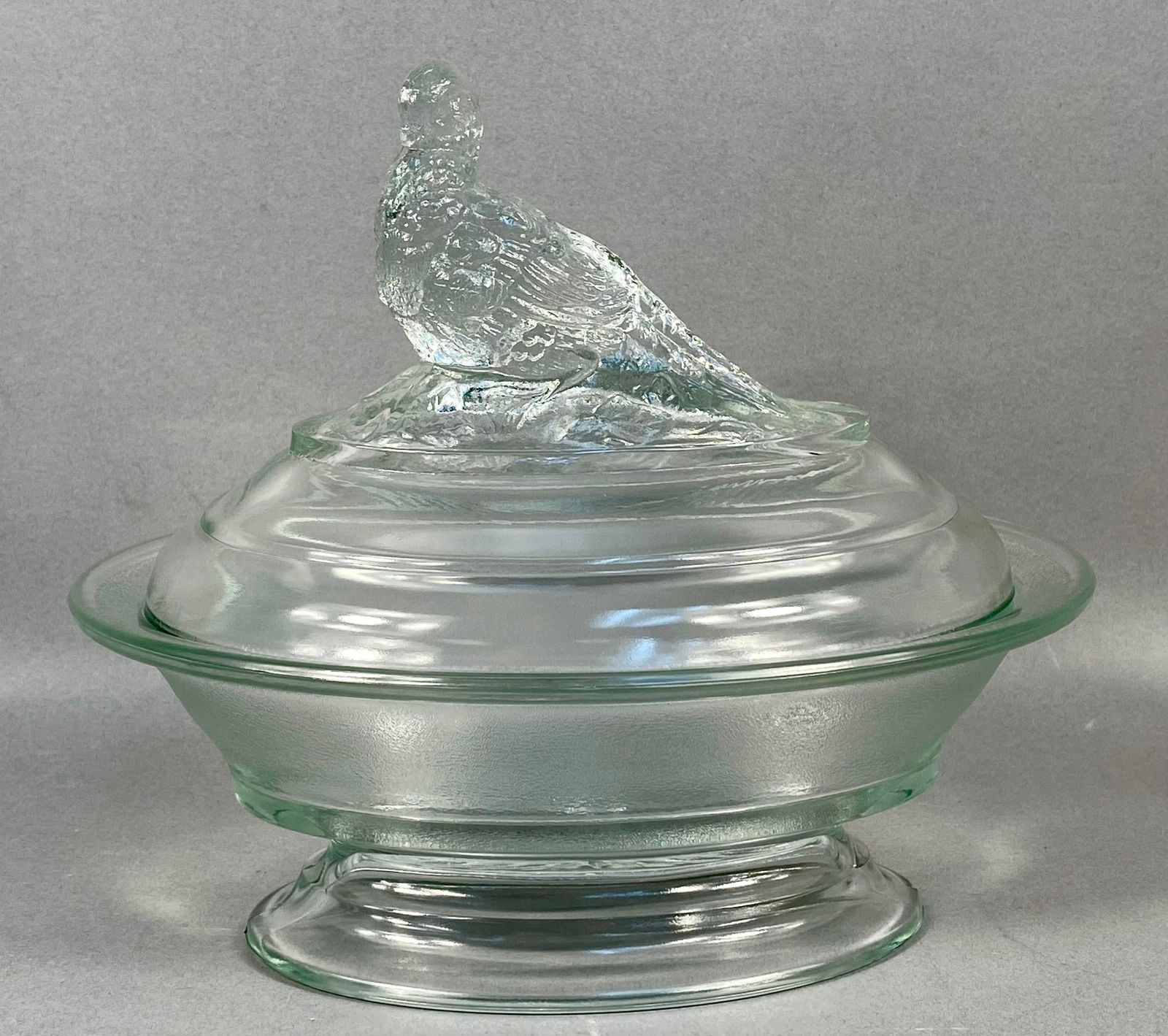 Imperial Glass Clear Pressed Glass Covered Compote with Quail Finial: This two-piece clear pressed glass covered compote is a product of the Imperial Glass Corporation. The decorative lid is designed with concentric molded rings and is surmounted by a textured figural f