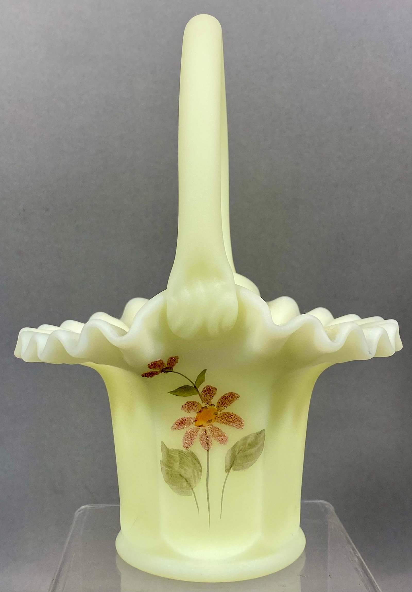 Fenton Hand Painted Custard Uranium Glass Basket for Tara Exclusive: A Fenton Art Glass Company custard glass basket featuring a heavily ruffled rim and an applied handle. The body of the vessel is molded with vertical ribs. The exterior is decorated with a hand-painte