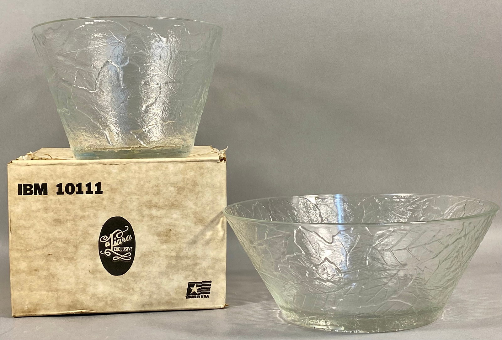 A Pair of Tiara Exclusives Clear Pressed Glass Leaf Pattern Bowls: A pair of clear pressed glass bowls featuring an all-over relief pattern of overlapping leaves, resembling maple or oak, set against a heavily textured background. The collection consists of two bowls