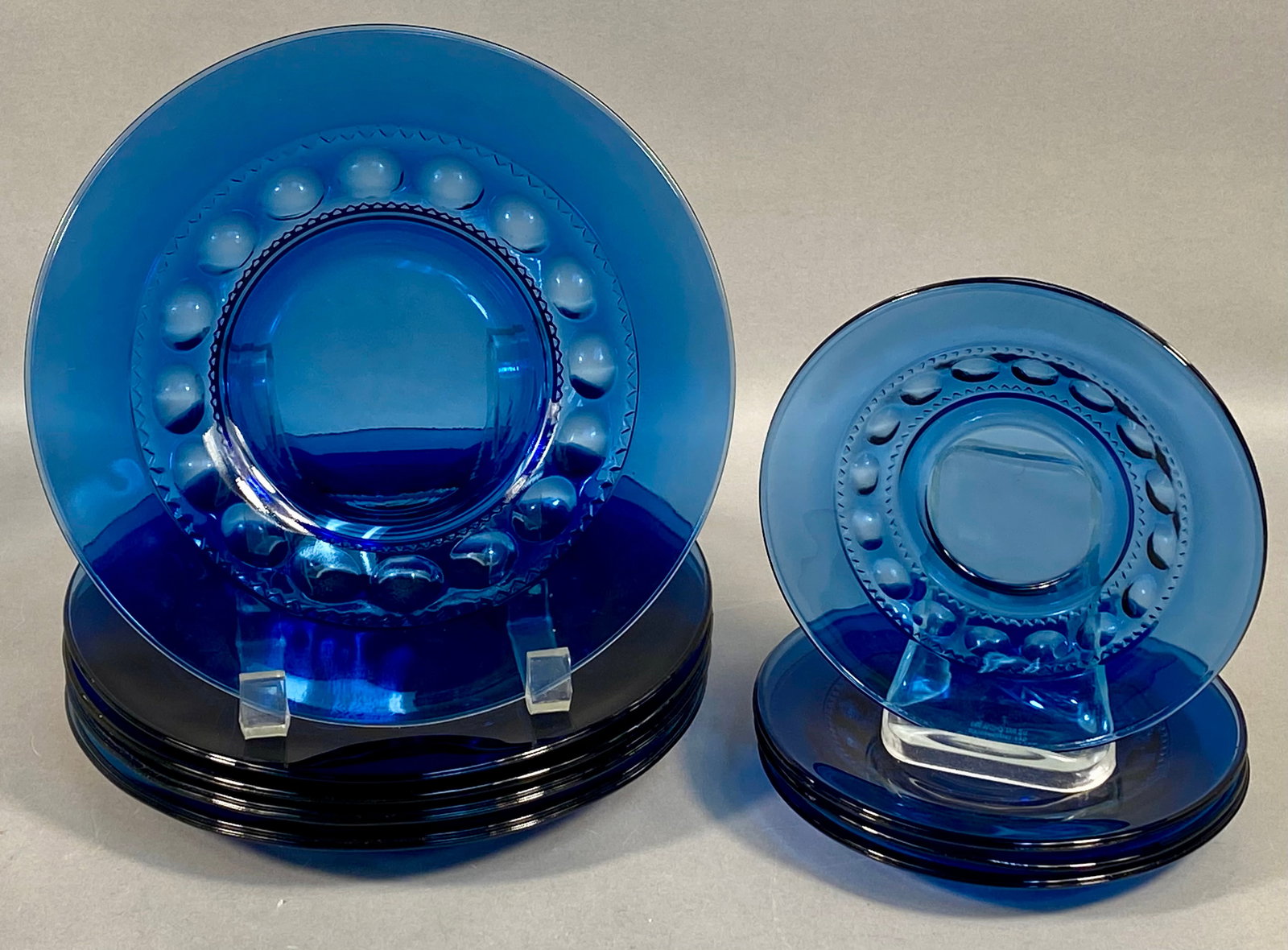 A Ten Piece Set of Tiara Crown Imperial Cobalt Blue Glass Plates: This set of ten cobalt blue pressed glass plates is in the Crown Imperial pattern, attributed to Tiara Exclusives. The design features a recessed central well surrounded by a band of circular thumbpri