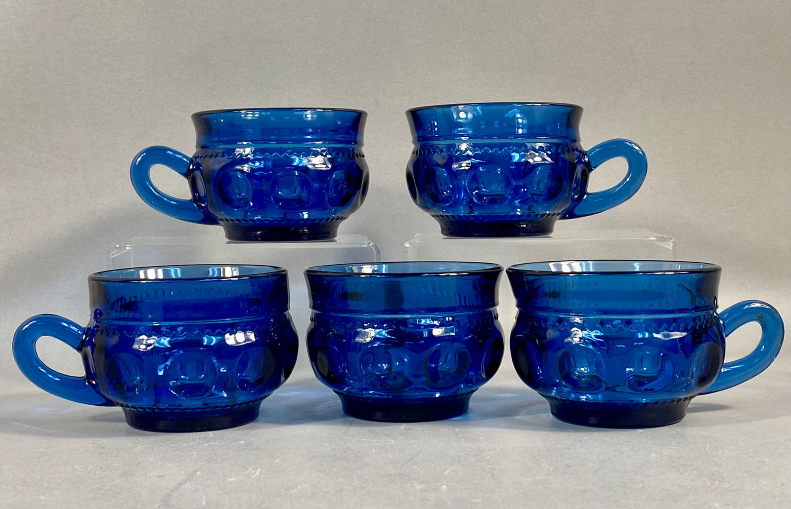 A Set of 5 Tiara Exclusive Crown Imperial Cobalt Blue Glass Cups: This set of five pressed glass cups is produced in the Crown Imperial pattern by Tiara Exclusive. Each piece is constructed from deep cobalt blue glass. The design features a row of large circular thu
