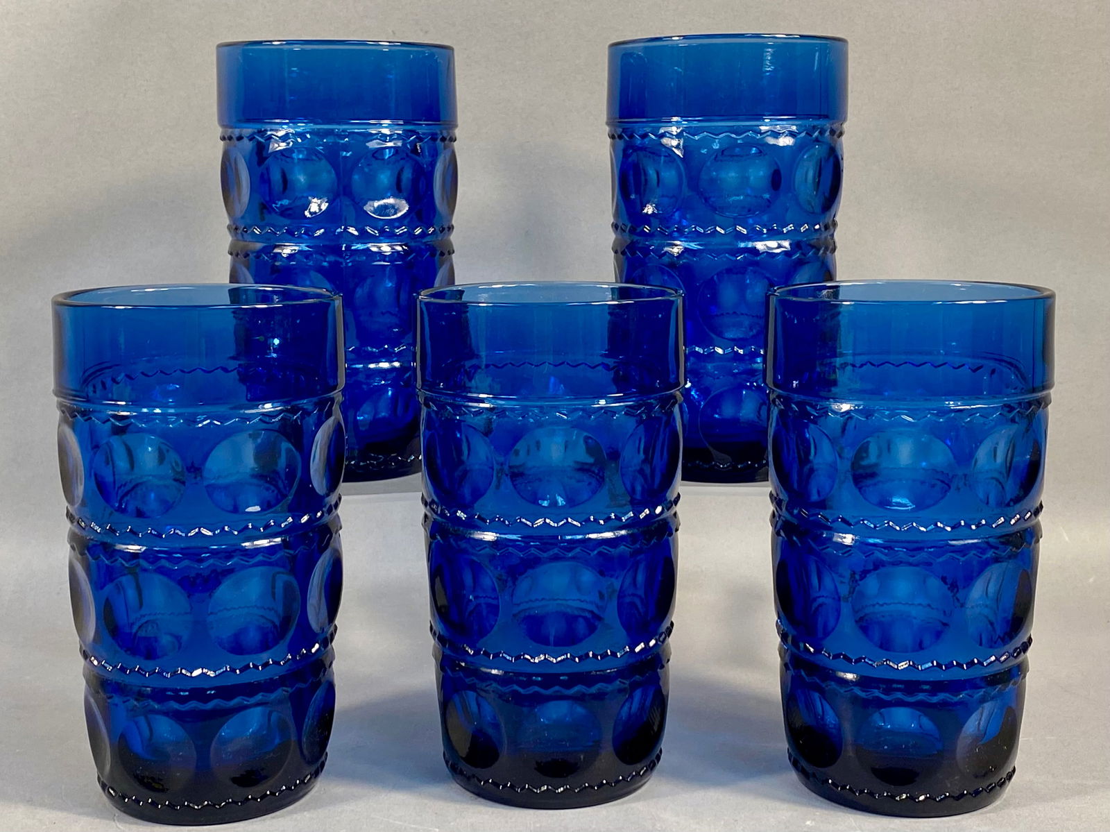 A Set of Five Tiara Crown Imperial Blue Glass Tumblers: A set of five pressed glass tumblers in the Crown Imperial pattern, attributed to Tiara Exclusives. The vessels are constructed from deep cobalt blue glass. The decorative scheme features three horizo