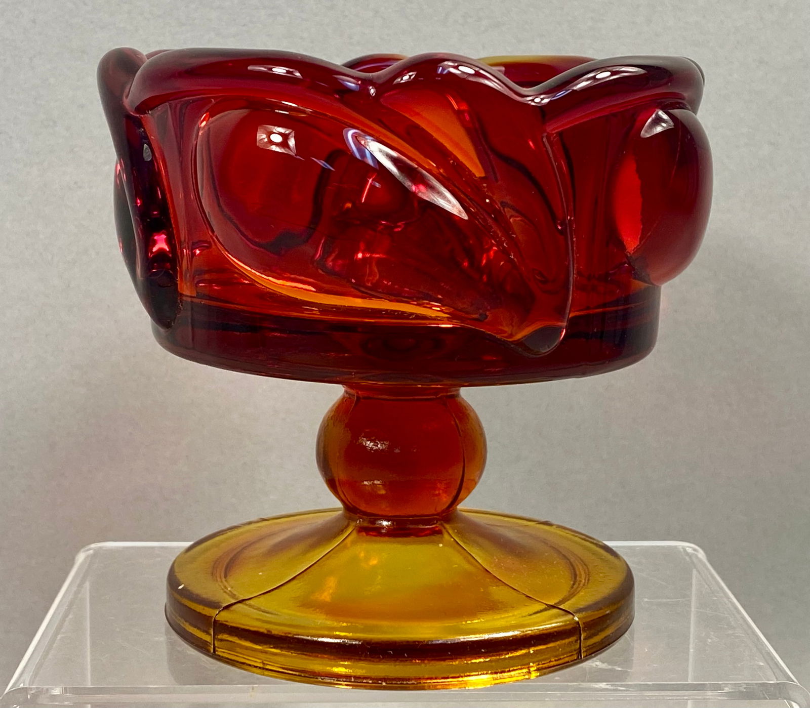 Tiara Exclusives Indiana Glass Leaf Pattern Sunset Amberina Footed Candle Holder: This footed candle holder was distributed by Tiara Exclusives and manufactured by the Indiana Glass Company in the Leaf pattern. The item is composed of Sunset Amberina glass, which exhibits a pressed