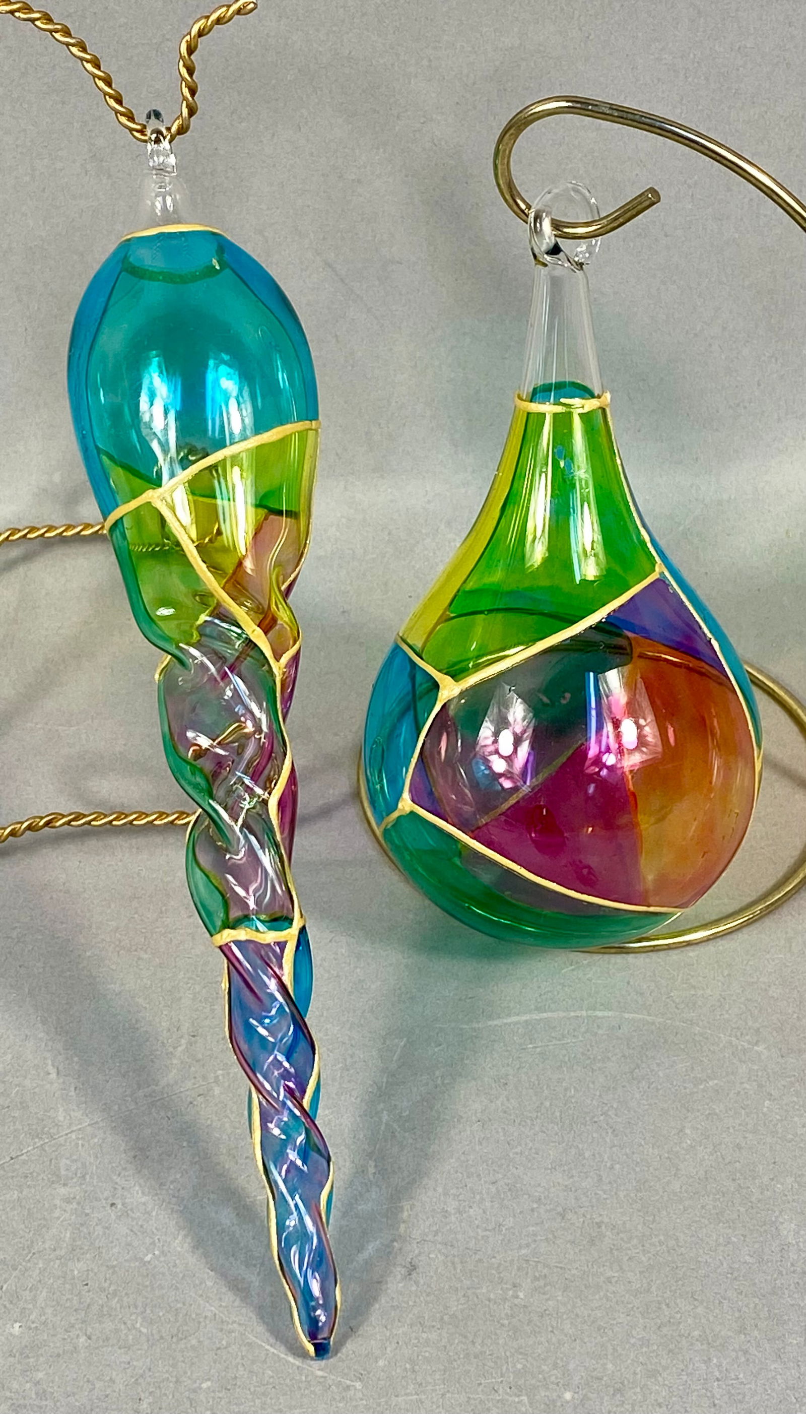 Two Hand-Blown Stained Glass Style Art Glass Ornaments: This lot consists of two hand-blown art glass ornaments featuring a decorative technique designed to mimic leaded stained glass. The first item is a teardrop or pear-shaped ornament crafted from trans