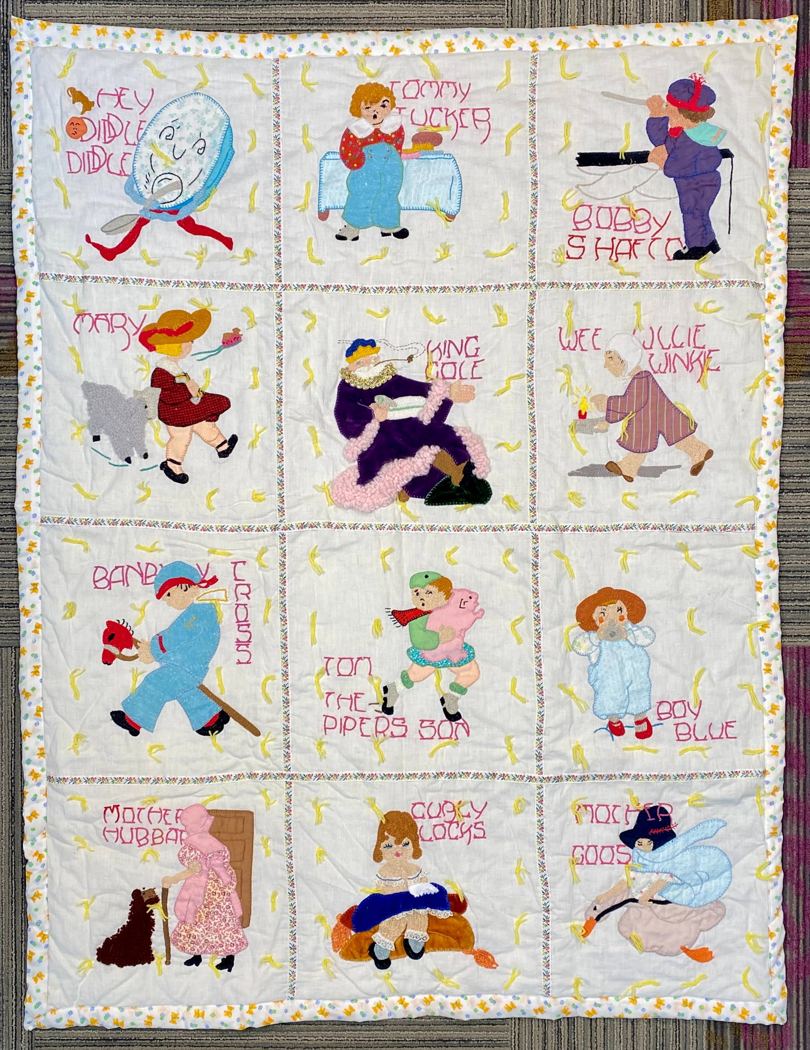 Jack Dempsey Needle Art Nursery Rhymes Appliqu?© and Embroidered Tied Nursery Quilt, 1989: This handmade tied nursery quilt features the Nursery Rhymes pattern by Jack Dempsey Needle Art. The quilt face is constructed from twelve rectangular panels, each depicting a classic Mother Goose cha