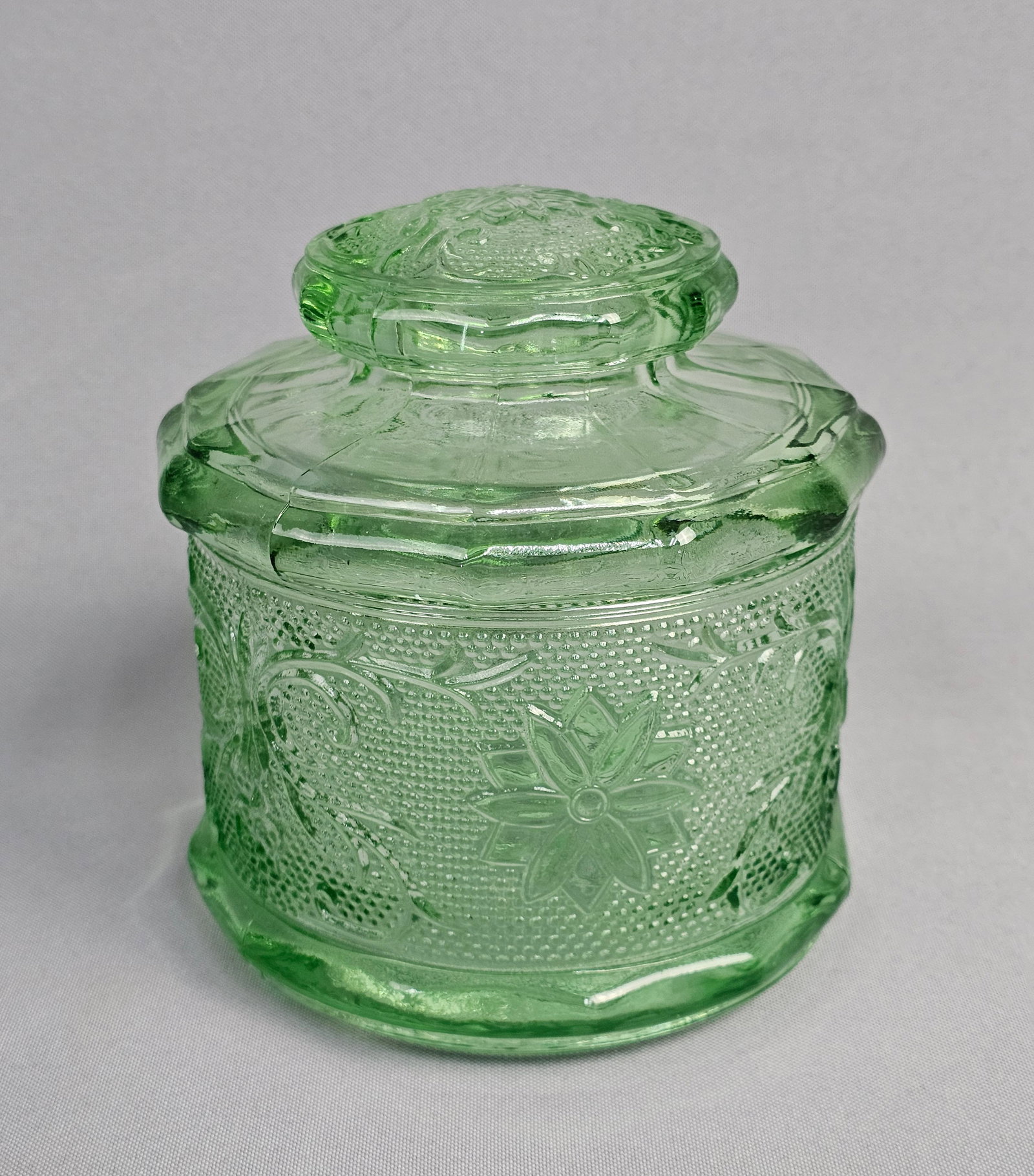 Tiara Exclusives Chantilly Green Glass Lidded Canister Jar: This lidded jar, typically used as a powder jar or puff box, is constructed from translucent green glass. No manufacturer marks or alphabetic characters are present on the piece. Diameter: 5 inches He