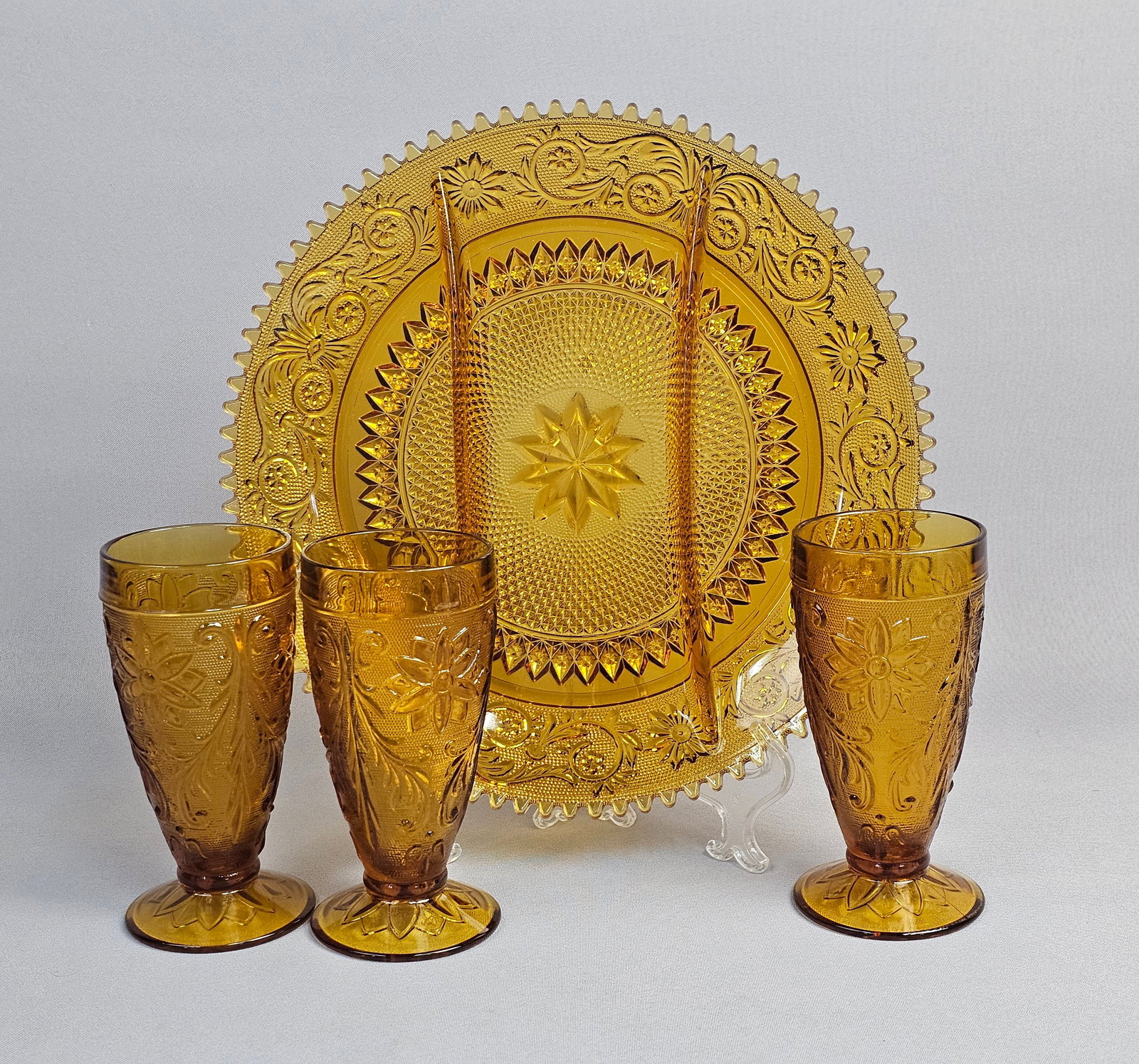 A Set of Indiana Glass Tiara Sandwich Pattern Amber Glass Serving Tray and Footed Tumblers: This set of pressed glass is manufactured by the Indiana Glass Company in the Sandwich pattern, a line frequently distributed by Tiara Exclusives during the mid-to-late 20th century. The glassware is